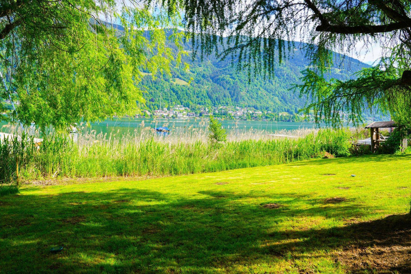 Weitläufiger Garten mit Rasenfläche und einem malerischen Blick auf den See und die bewaldeten Berge.
