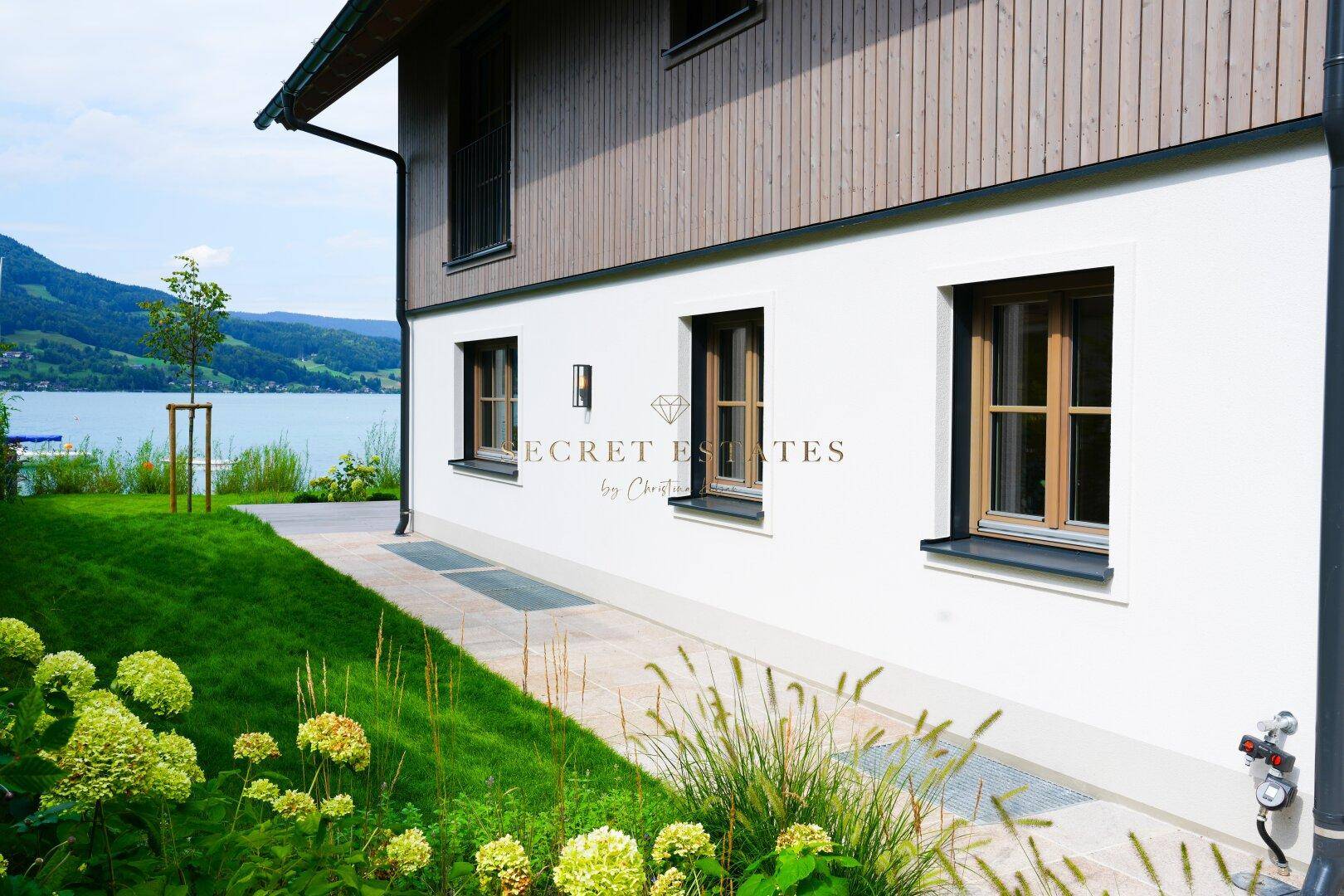 Moderne Hausfassade mit Holzverkleidung und Blick auf den See und die Berge.
