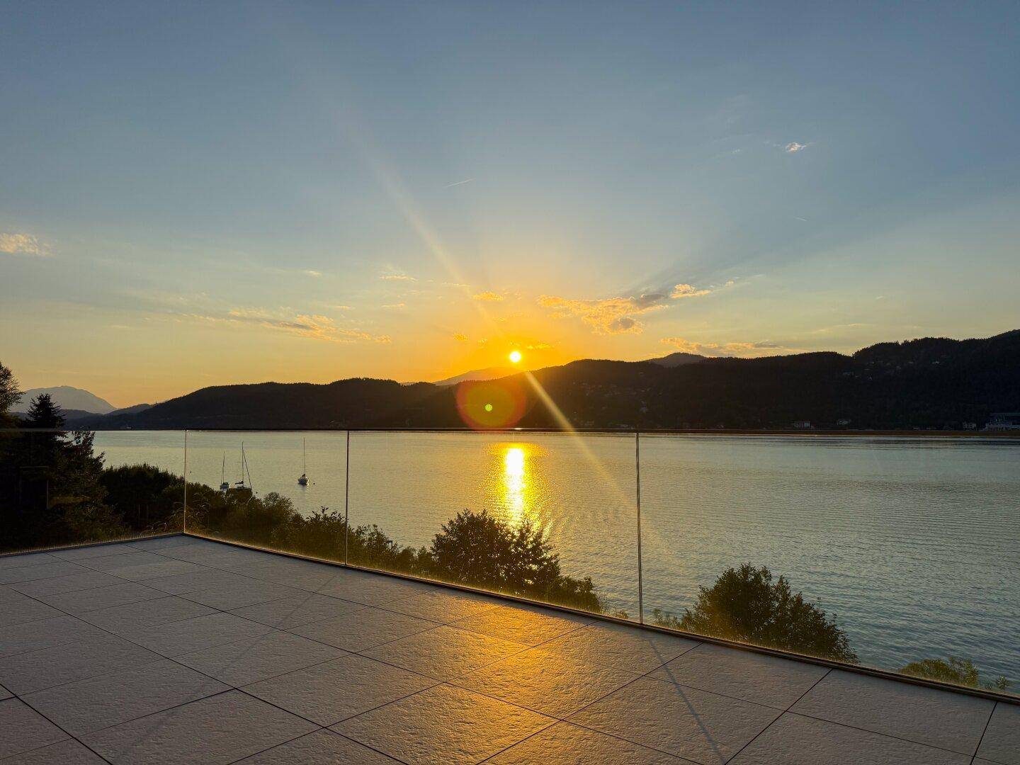 Großzügige Terrasse mit modernem Glasgeländer und weitem Blick über den See bei Sonnenuntergang.