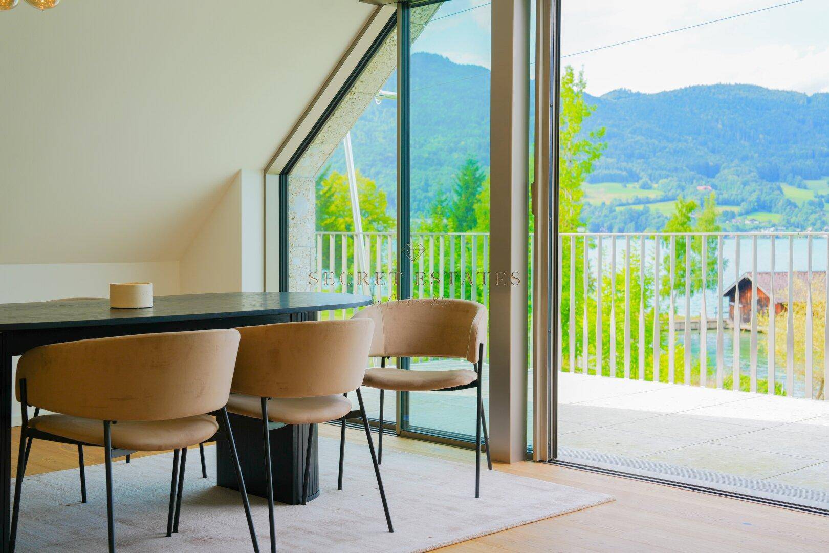 Heller Essbereich mit modernem Tisch und Stühlen, großen Fenstern, Dachschräge und beeindruckendem Seeblick.