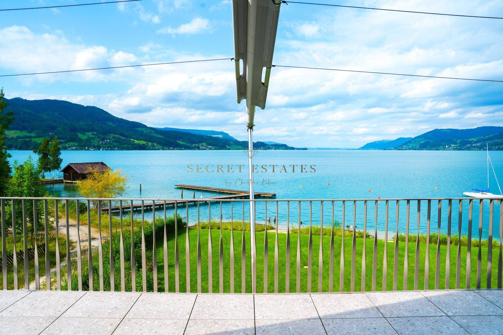 Große Terrasse mit weitem Blick auf den See, die Berge und eine grüne Wiese.