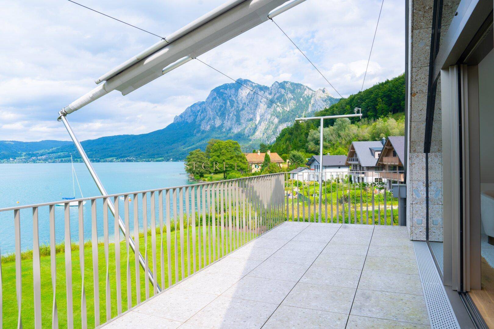 Geräumige Terrasse mit Fliesenboden, Blick auf den See und die umliegende Berglandschaft.