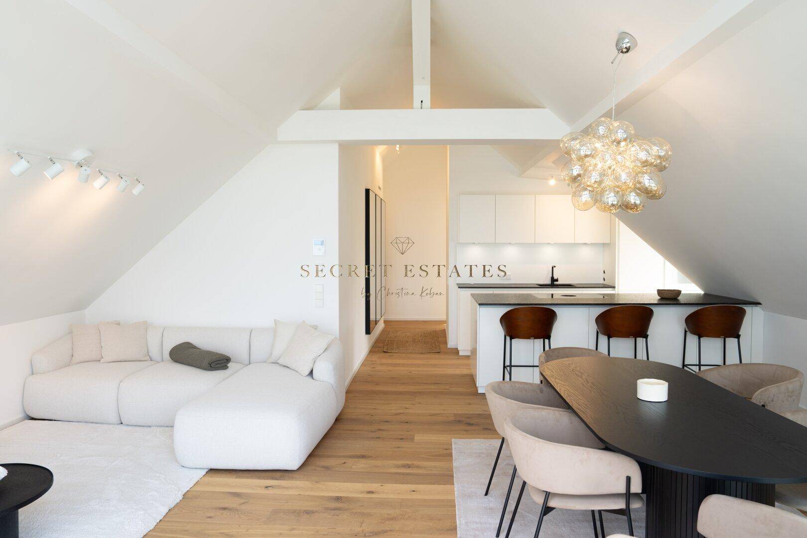 Offener Wohn-Essbereich mit moderner Küche, Sofa und hohen Decken unter schrägem Dach.
