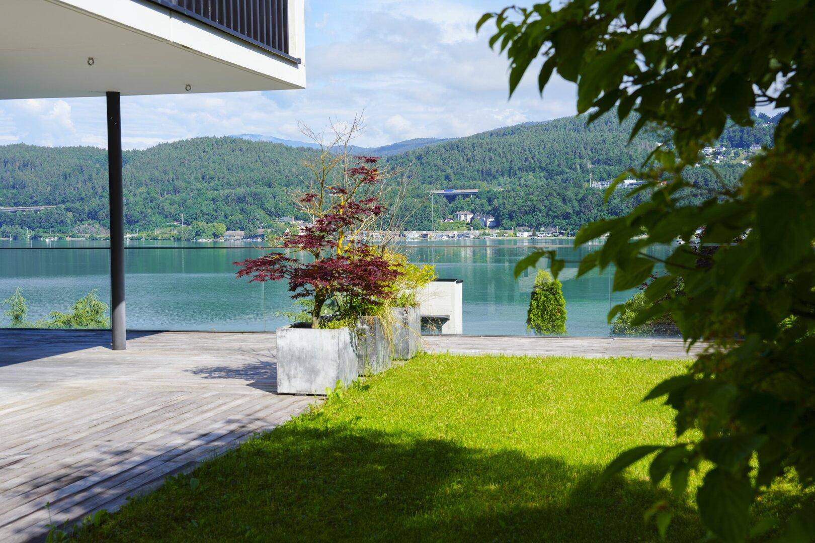 Holzterrasse und Rasenfläche mit atemberaubendem Blick auf den See und die umliegenden Berge.