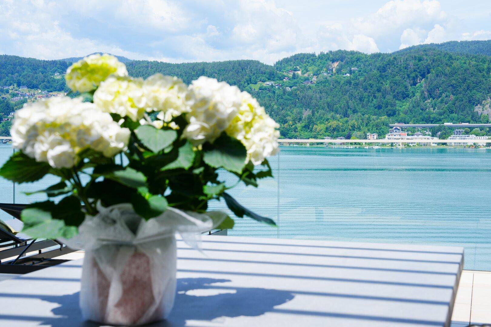 Sonnenverwöhnter Balkon mit atemberaubendem Blick auf den See und die umliegenden Berge, dekoriert mit Blumen.