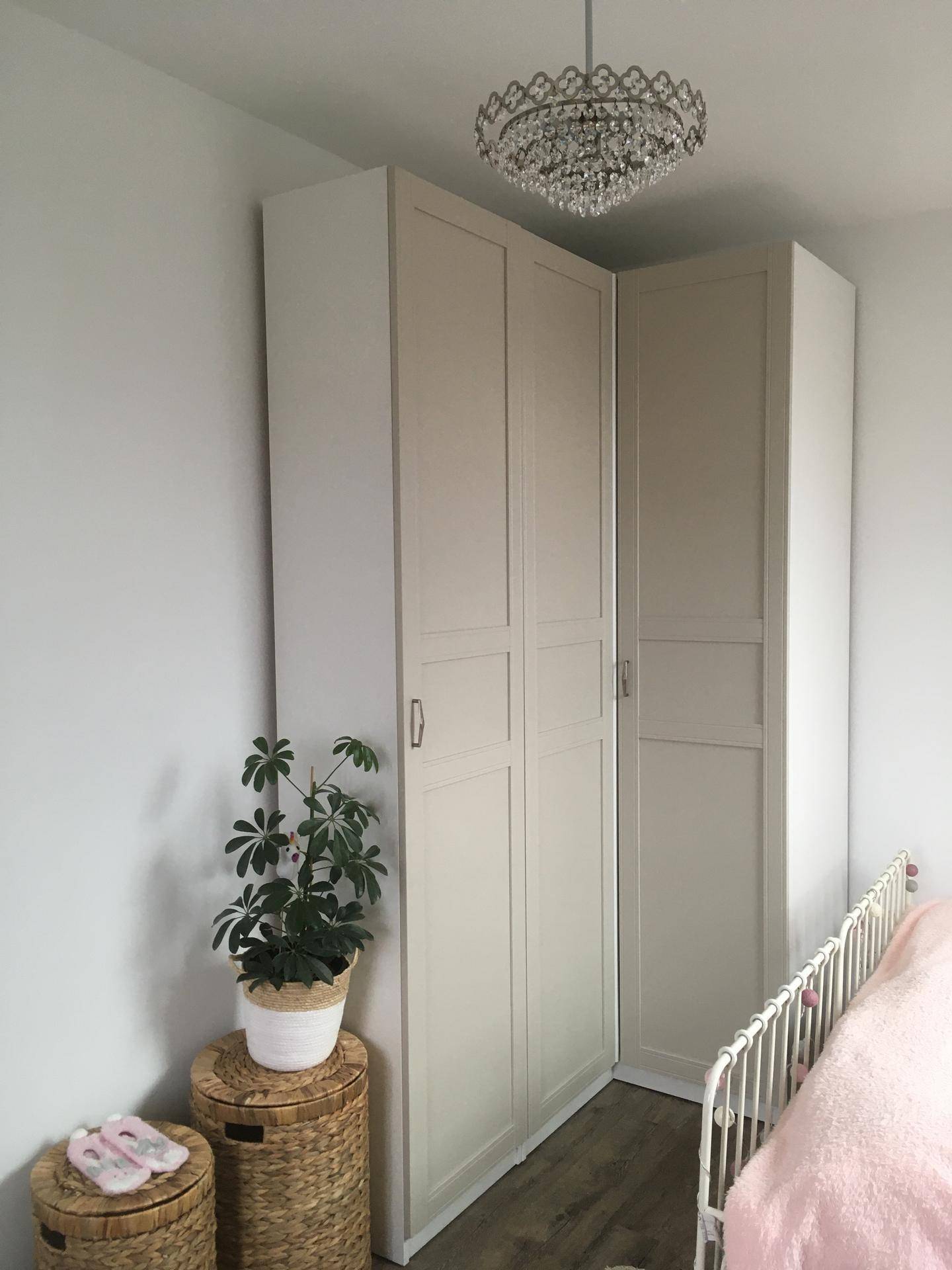 Schlafzimmer mit Eckkleiderschrank, Pflanzen und Kronleuchter, in hellen Farbtönen gehalten.