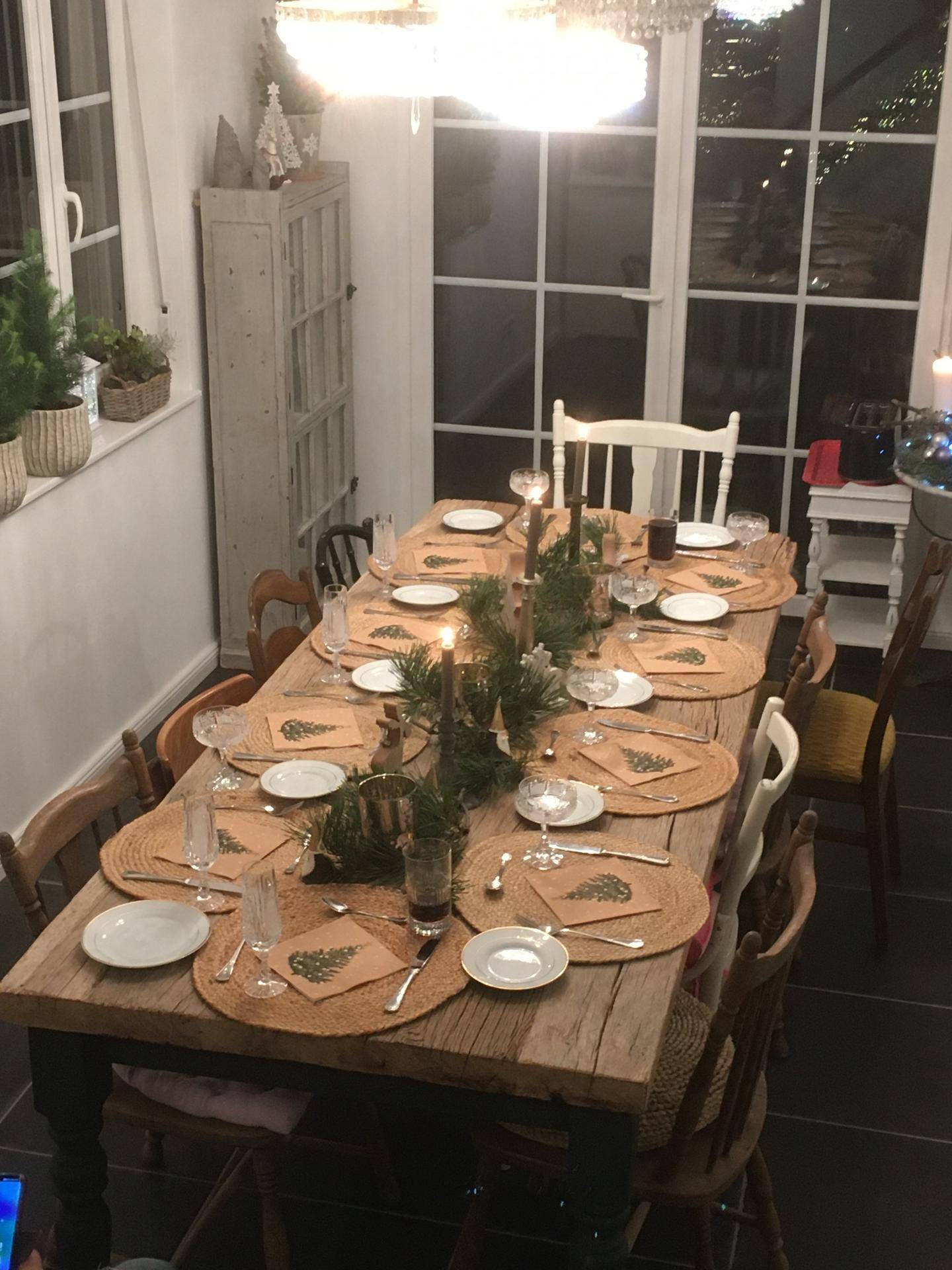 Großer Holztisch mit festlicher Dekoration und Blick auf den Garten durch die Fenster.