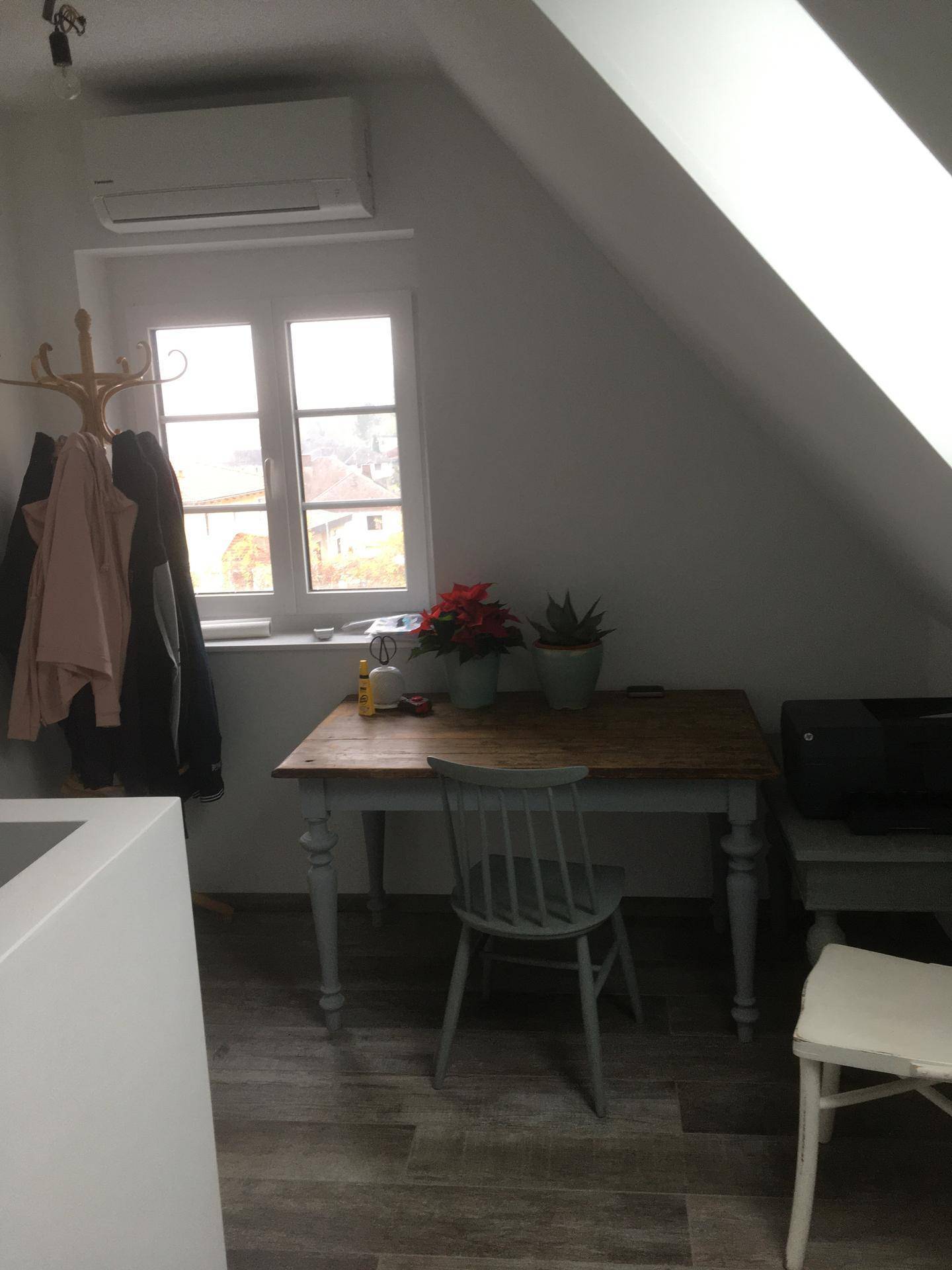 Dachzimmer mit Schreibtisch, Stuhl, Klimaanlage und Fenster mit Ausblick.