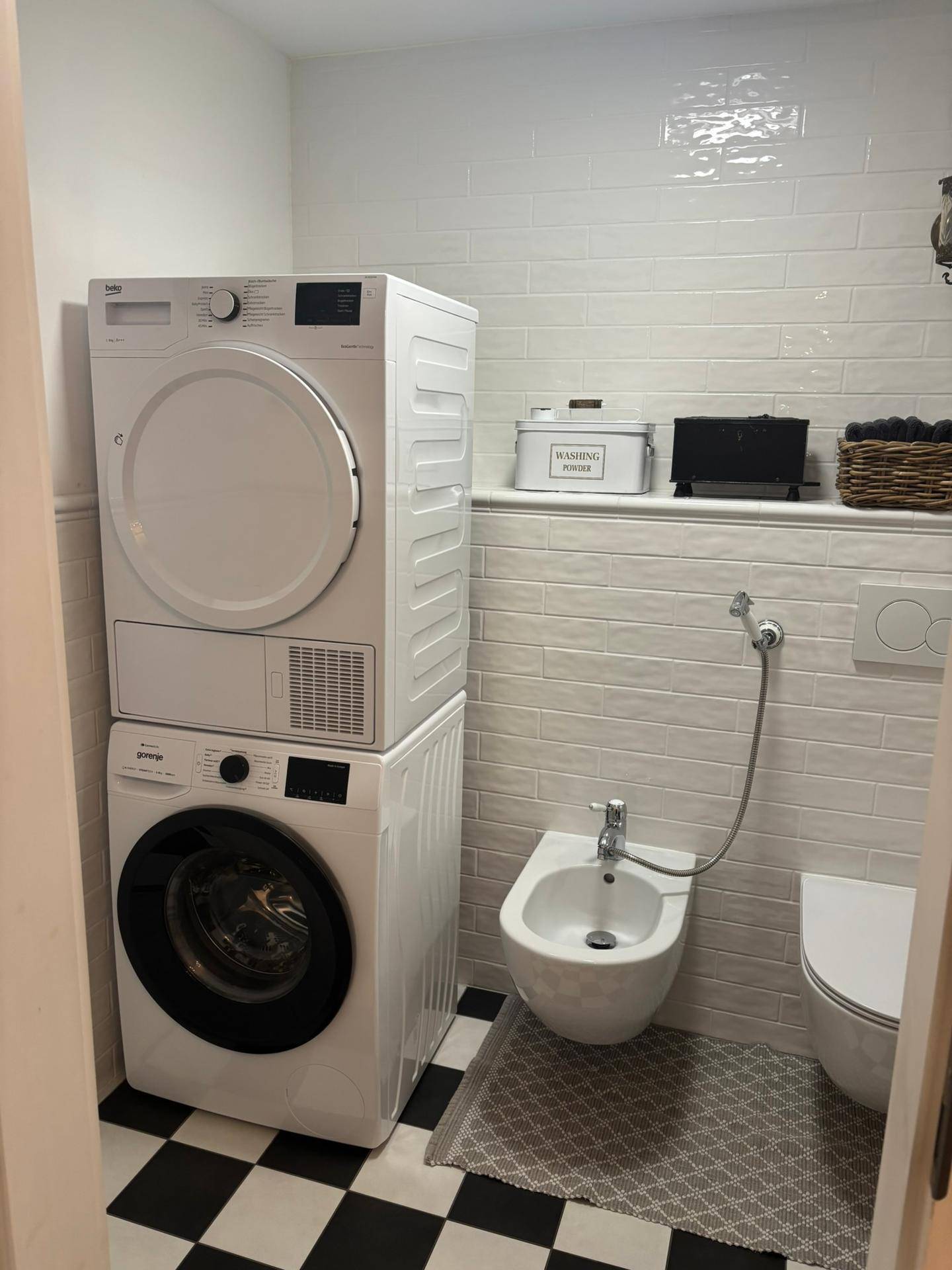 Waschraum mit Waschmaschine, Trockner, Bidet und WC, ausgestattet mit weißen Fliesen.