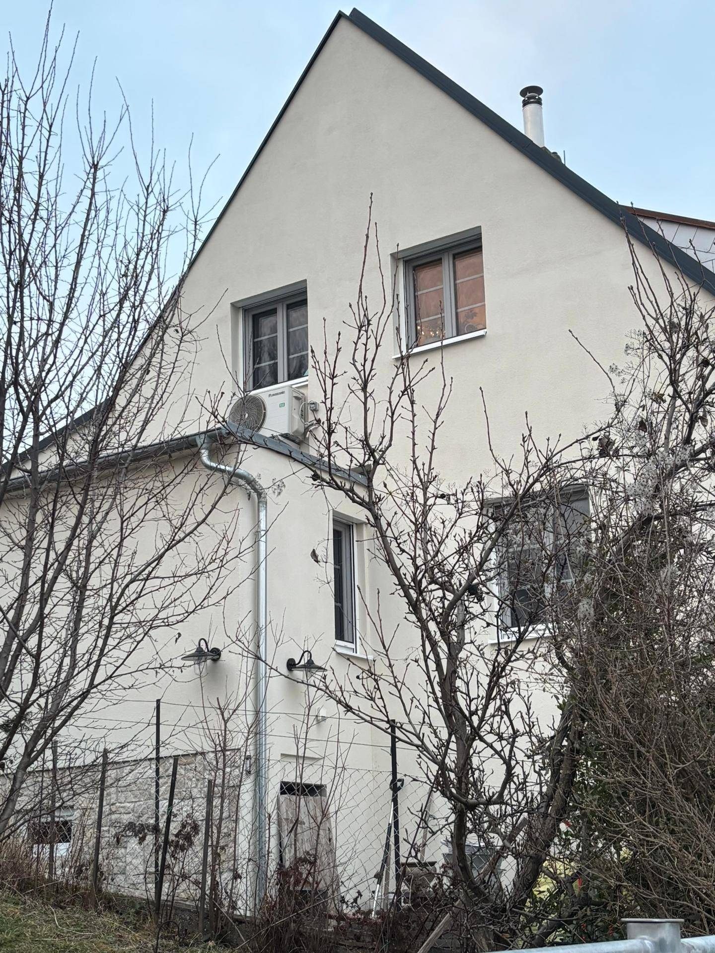 Seitenansicht des Hauses mit Giebeldach, Fenstern und einer Klimaanlage an der Fassade.