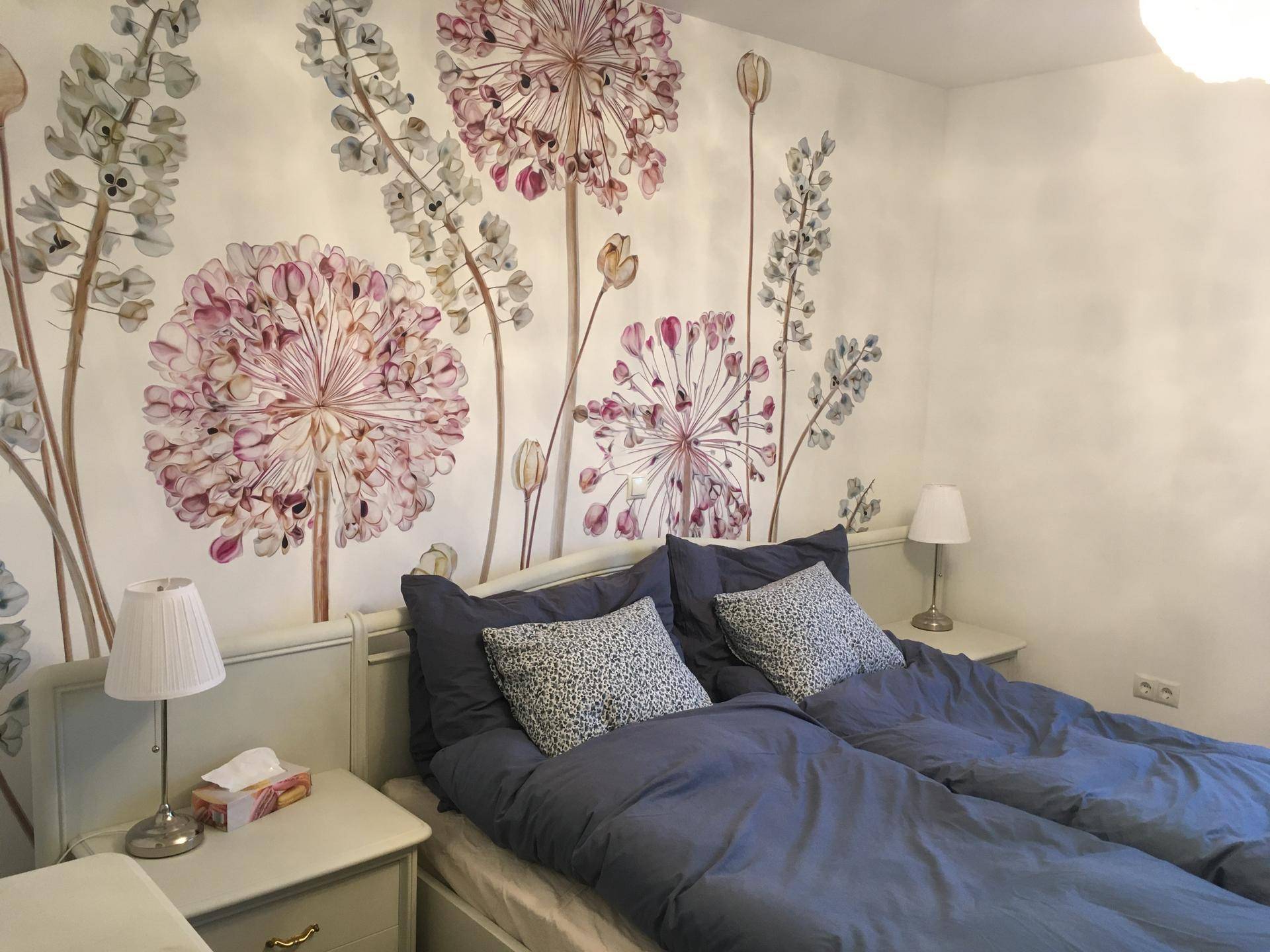 Schlafzimmer mit floraler Wanddekoration, Doppelbett und Nachttischen mit Lampen.