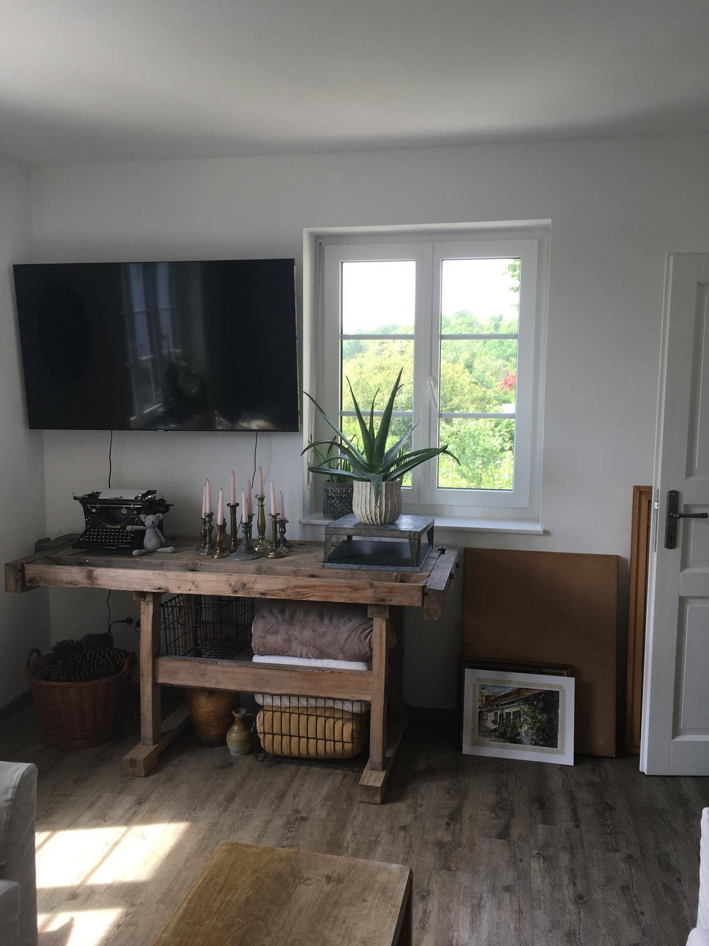 Wohnzimmer mit Holztisch, Fernseher an der Wand und Blick ins Grüne durch das Fenster.