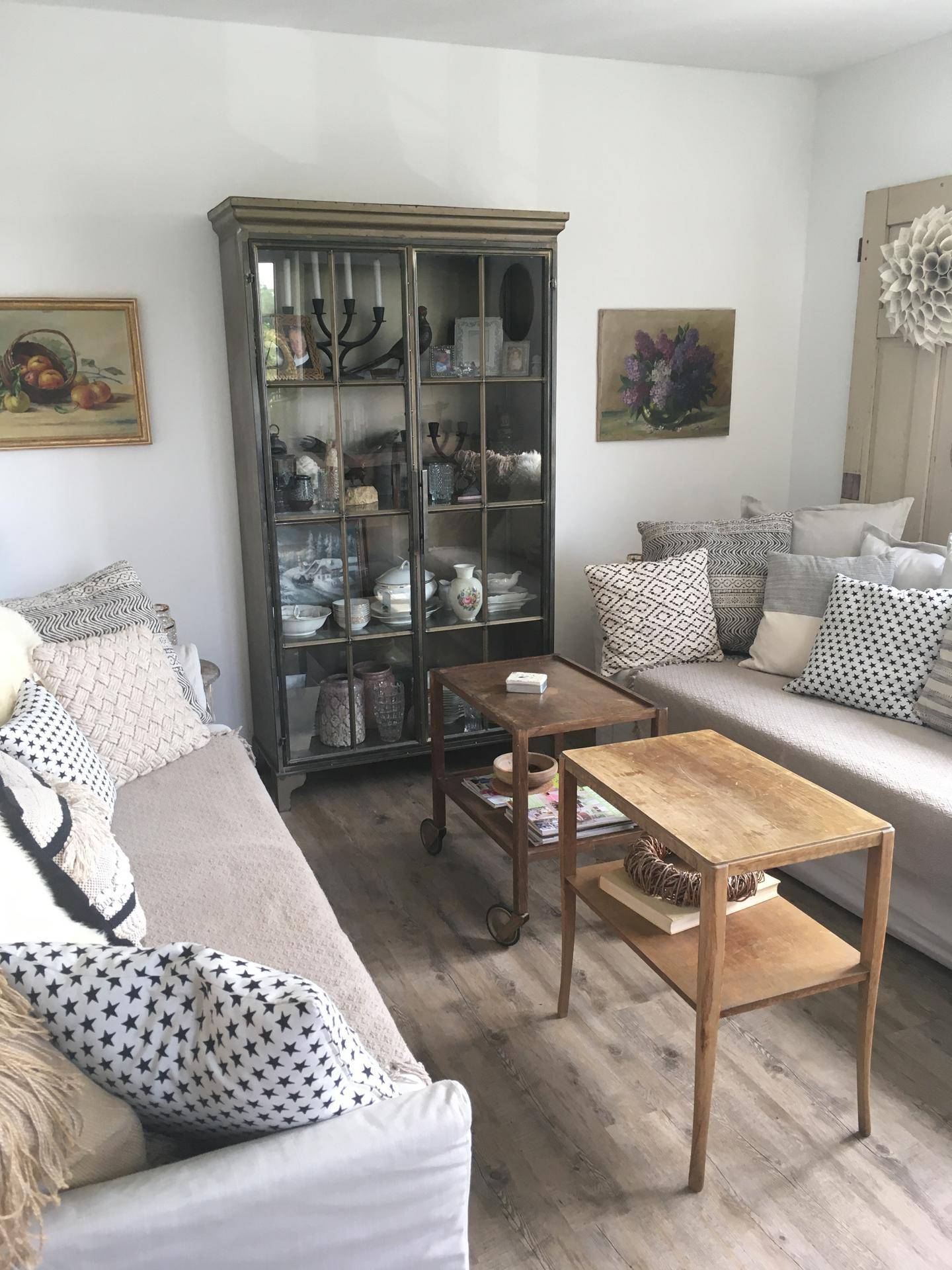 Gemütliches Wohnzimmer mit zwei Sofas, Holztischen und einem Vitrinenschrank.