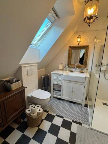 Badezimmer im Dachgeschoss mit WC, Waschbecken, Spiegel und Dachfenster für Tageslicht.