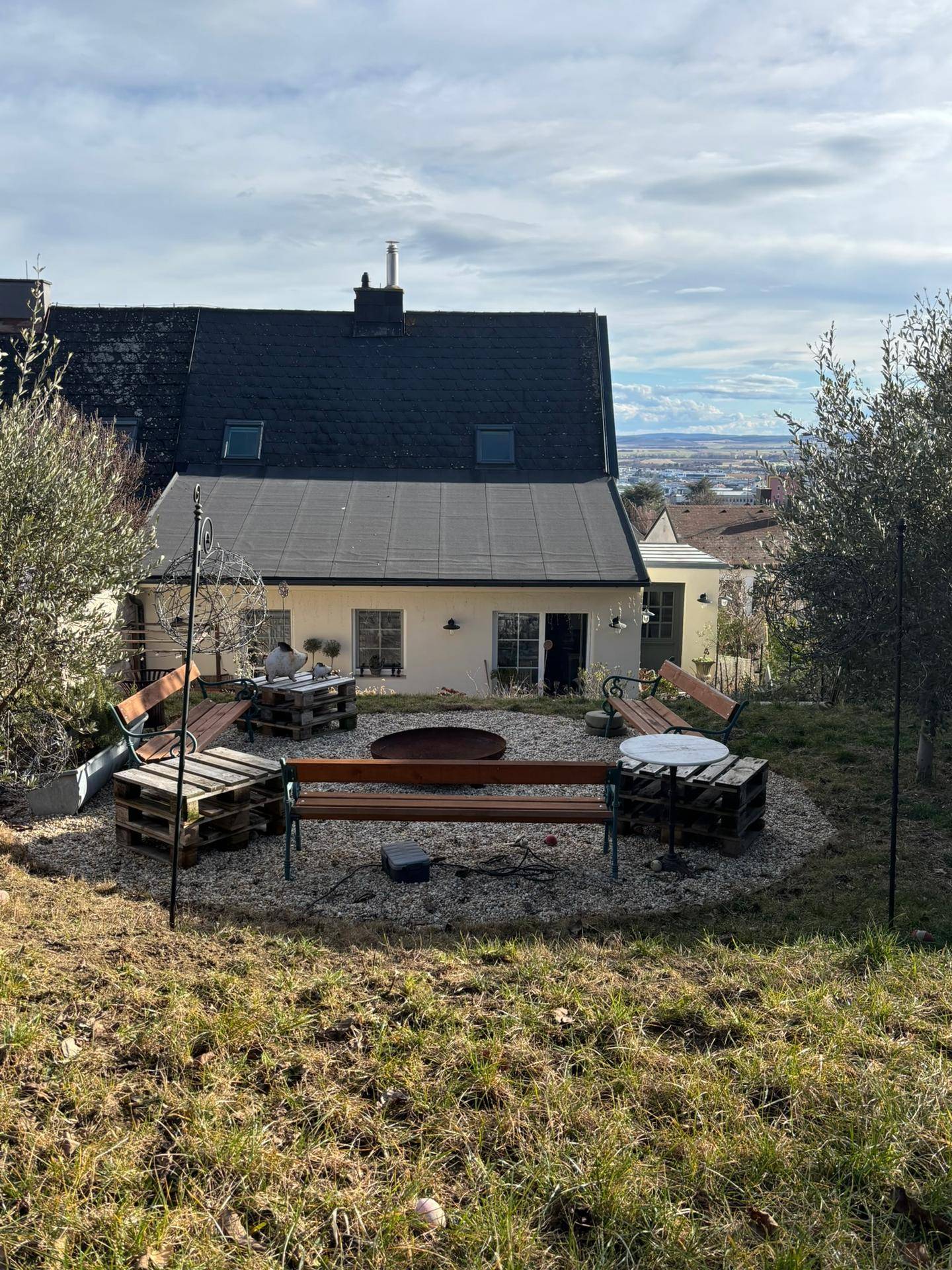 Gartenbereich mit Sitzgelegenheiten, Feuerstelle und Blick auf das Haus und die Landschaft.