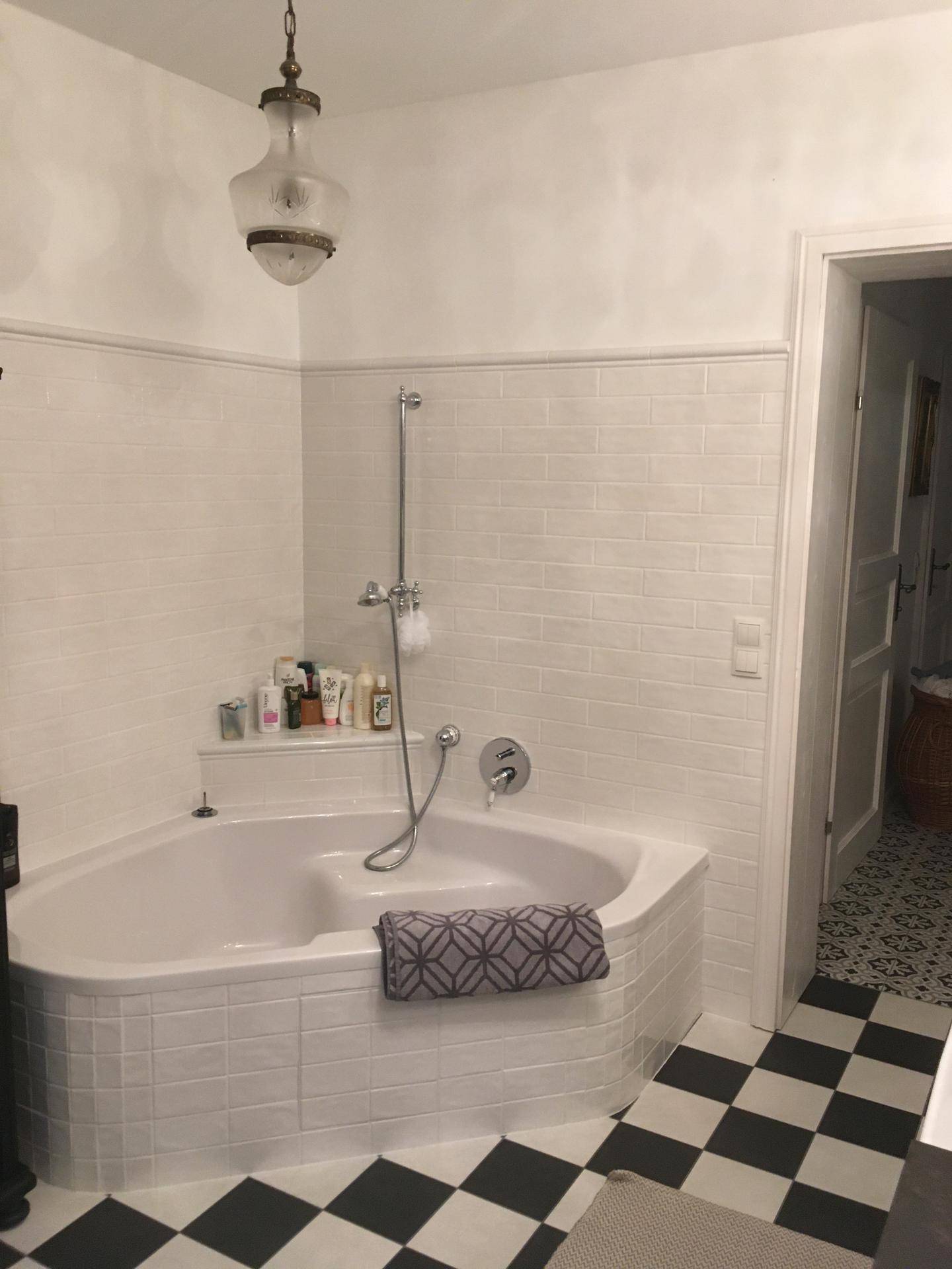 Badezimmer mit Eckbadewanne, weißen Fliesen und schwarz-weißem Schachbrettmuster auf dem Boden.