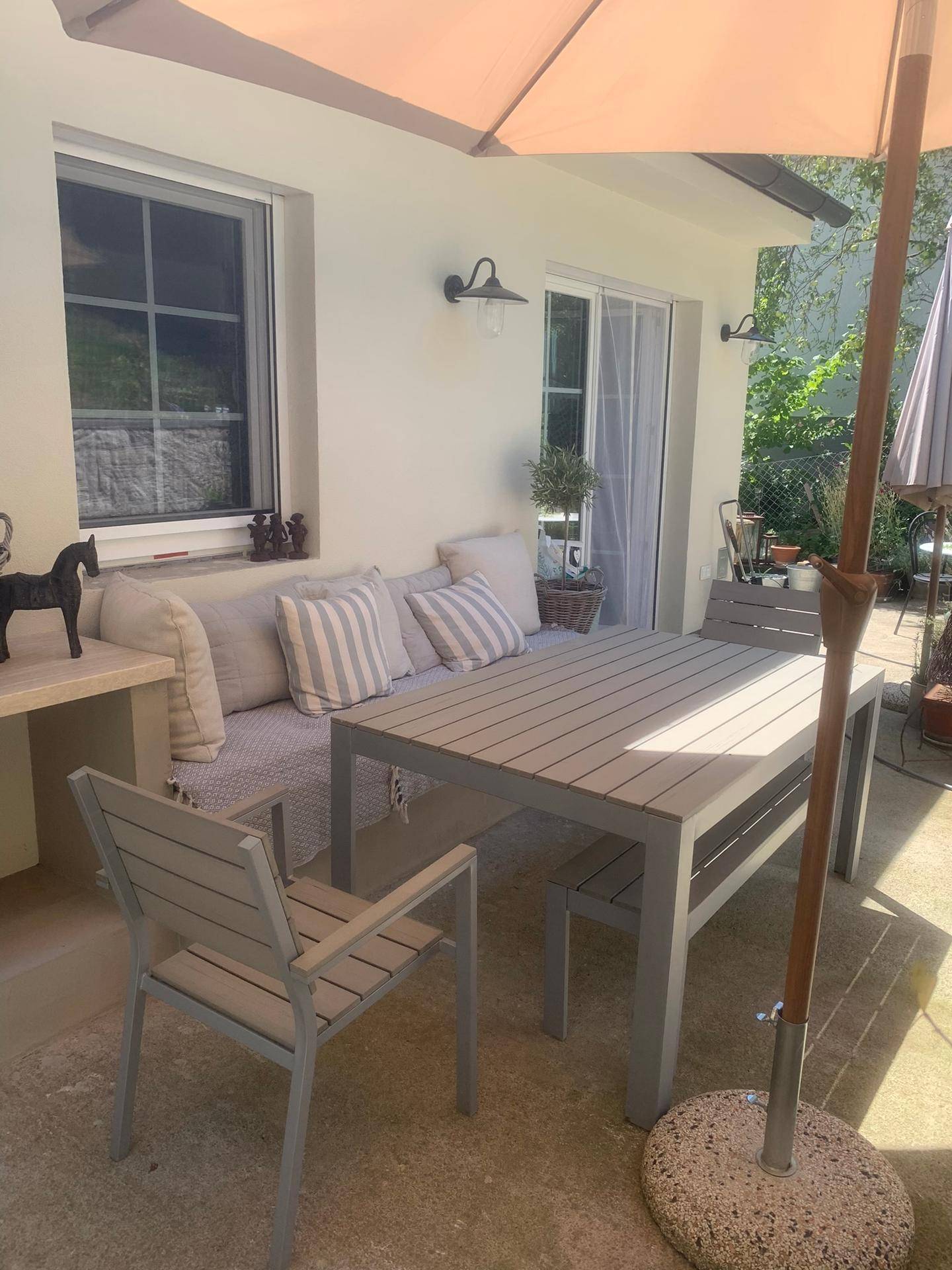 Sonnige Terrasse mit Esstisch, Stühlen und Sonnenschirm, ideal für Mahlzeiten im Freien.