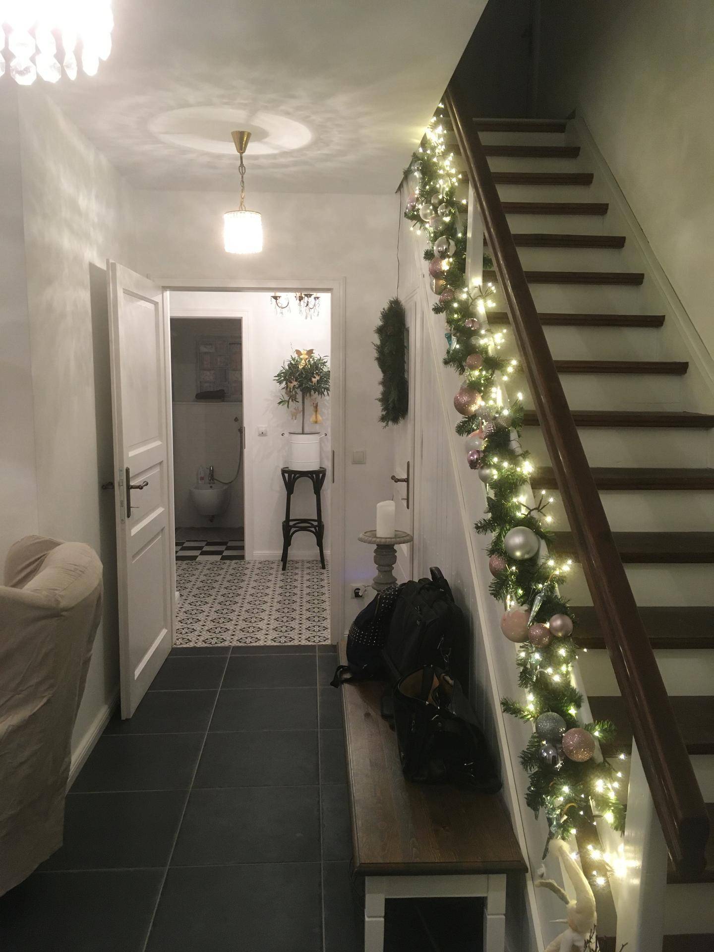 Treppenhaus mit festlicher Weihnachtsdekoration, dunklen Fliesen und Zugang zu weiteren Räumen.