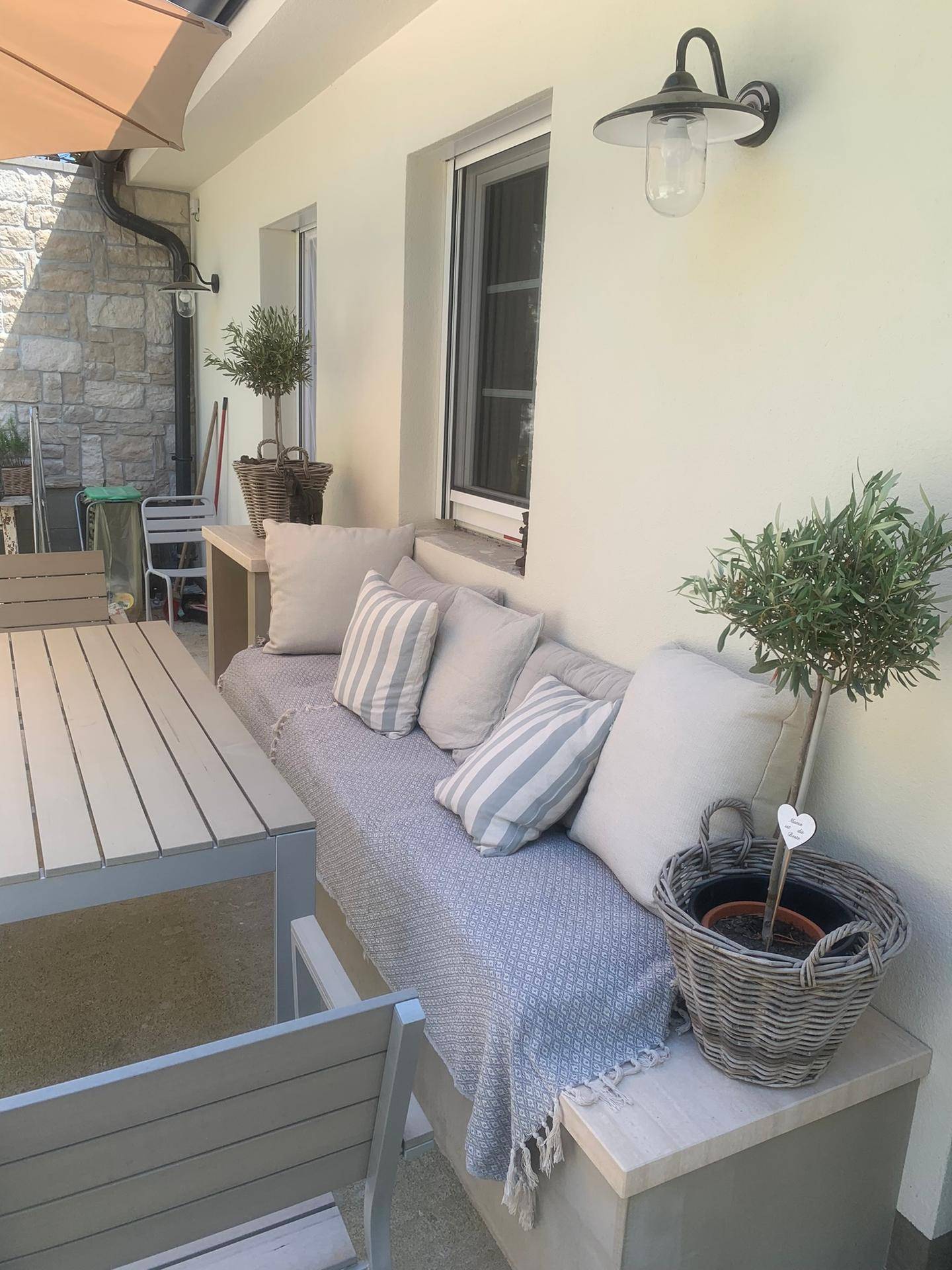 Gemütliche Terrasse mit Sitzbank, Kissen und Esstisch für entspannte Stunden im Freien.