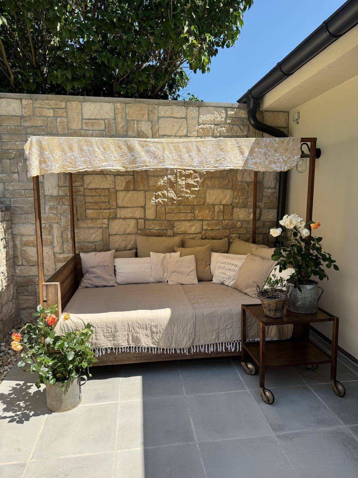 Entspannungsbereich auf der Terrasse mit Tagesbett, Kissen und Steinwand im Hintergrund.