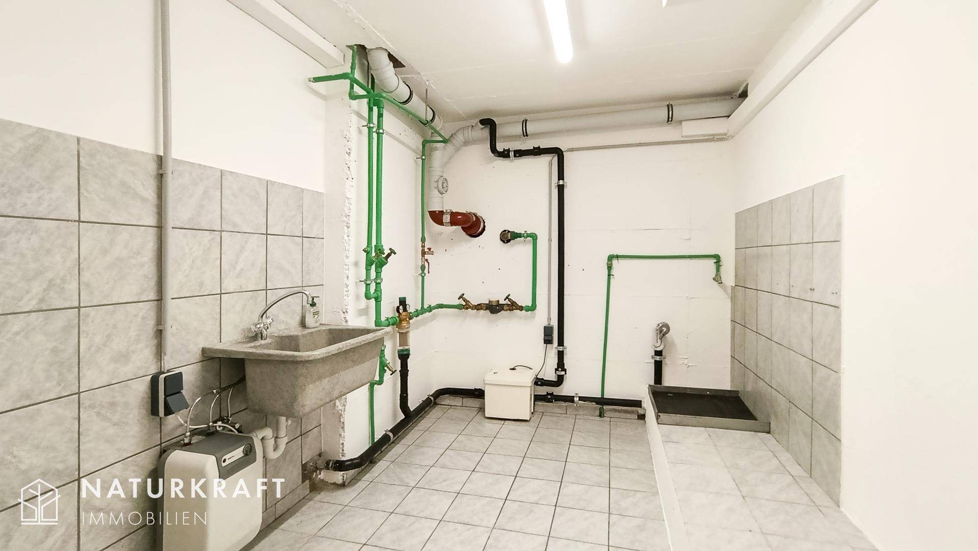 Funktionaler Hauswirtschaftsraum im Keller mit Waschbecken und sichtbaren Installationen.