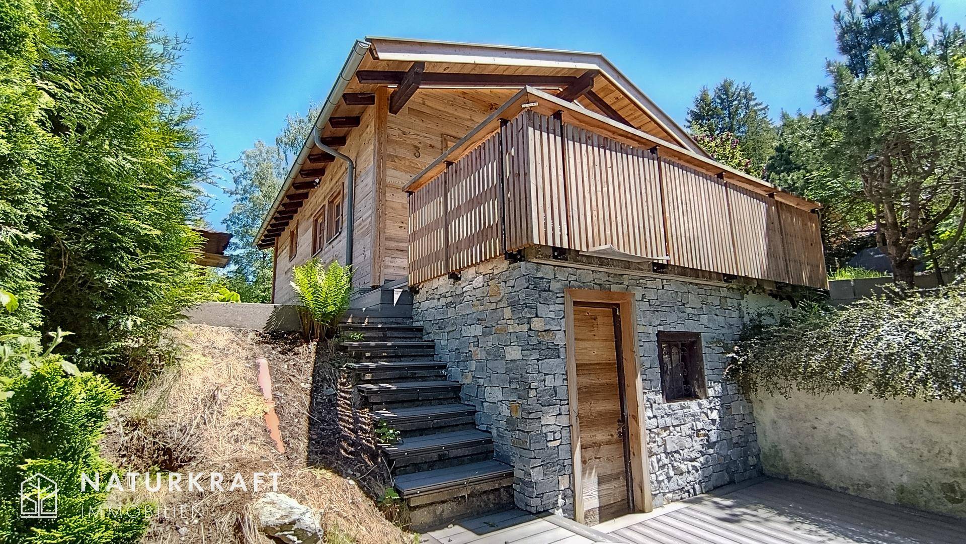 Rustikales Holzchalet mit Steinfundament und Außentreppe, harmonisch in die Natur eingebettet.
