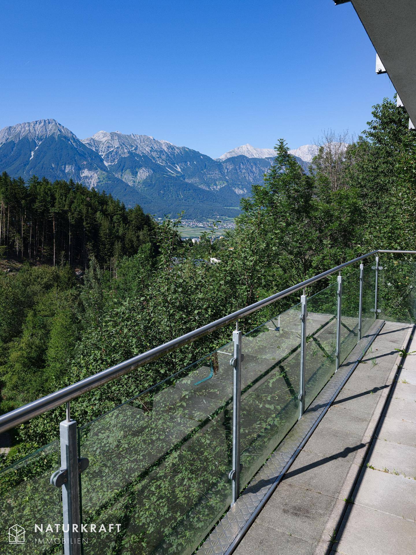 Balkon mit Glasgeländer und weitem Blick auf die bewaldeten Berge und das Tal.