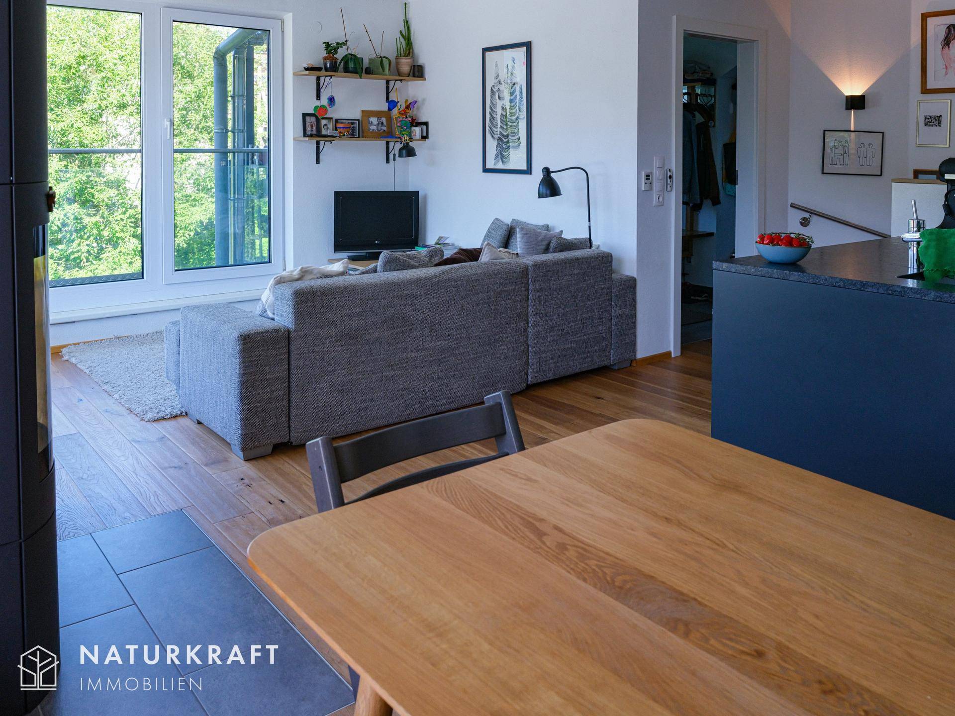 Heller Wohnbereich mit Esstisch, Sofa und Blick auf den Außenbereich durch große Fenster.