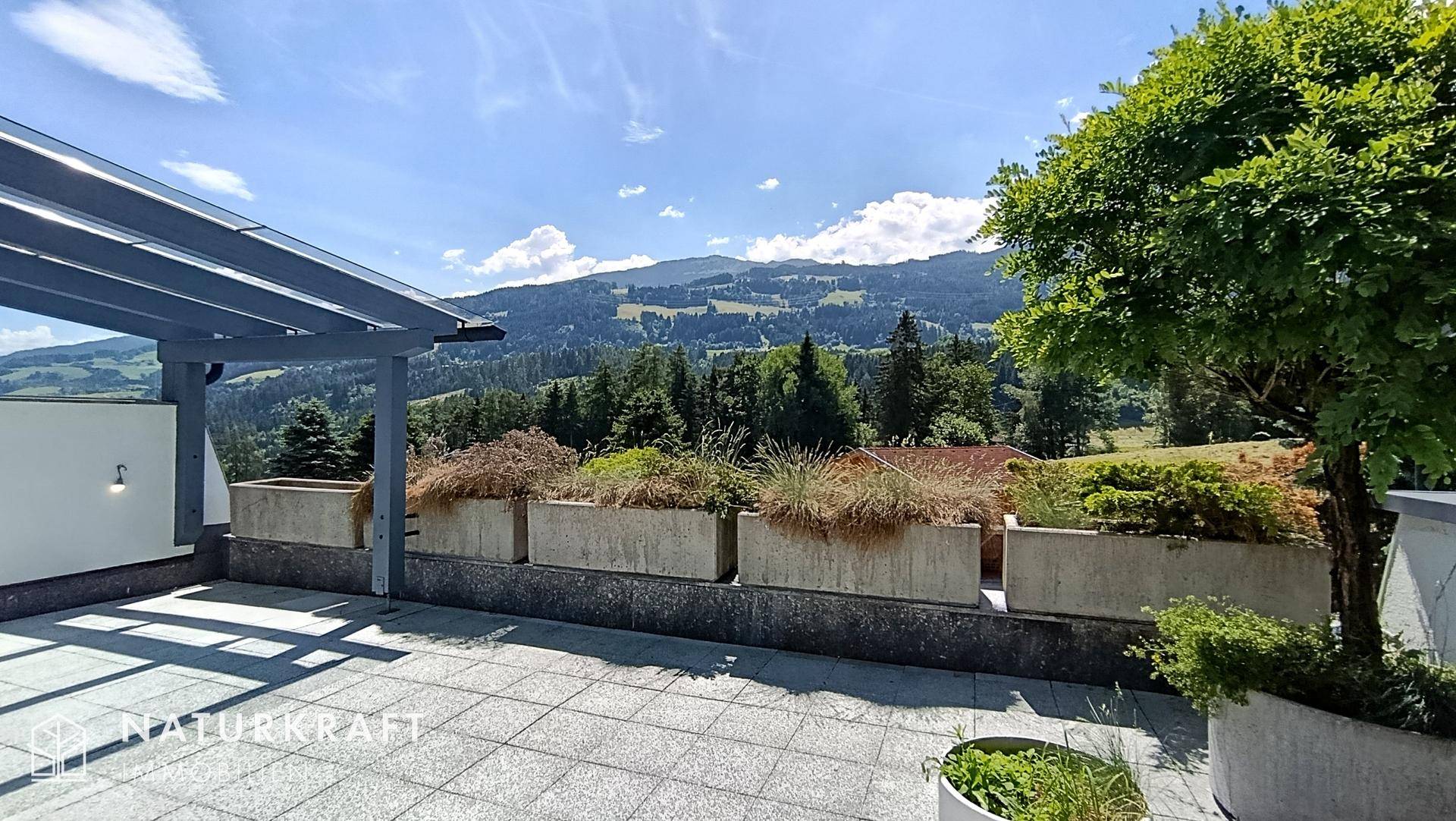 Große Dachterrasse mit Fliesenboden, Bepflanzung und Panoramablick auf die Berge.