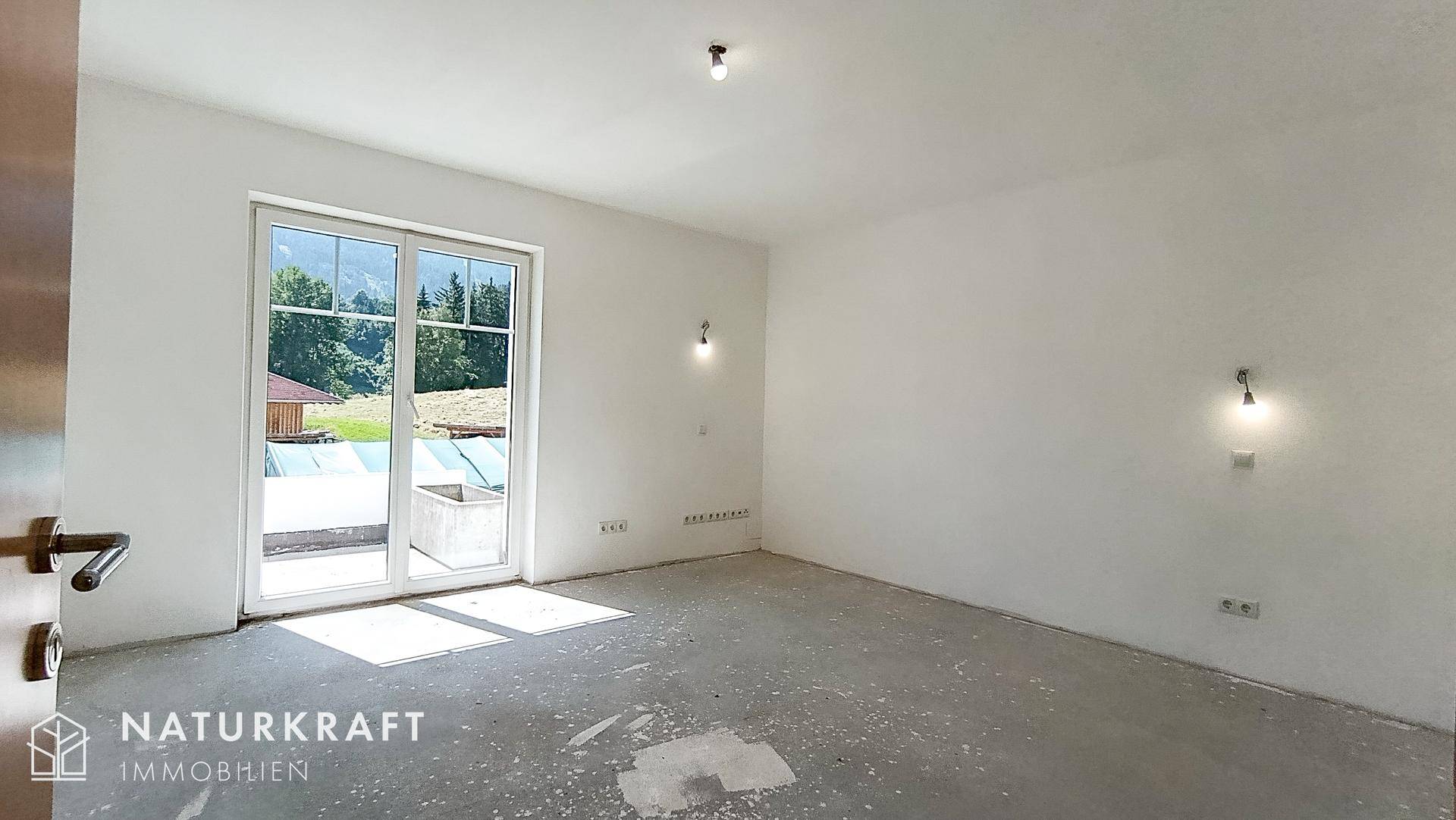 Leerer Raum mit Betonboden und großen Schiebetüren, die viel Tageslicht hereinlassen.