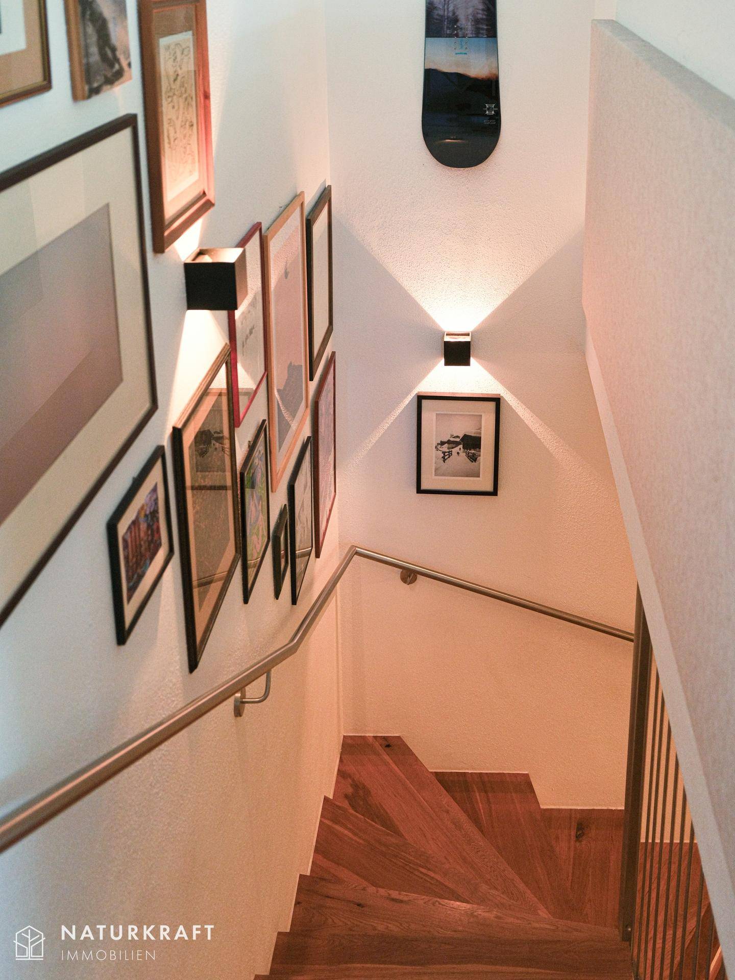 Treppenhaus mit Holzstufen, modernem Geländer und gerahmten Bildern an der Wand.