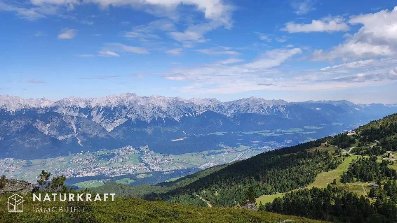 Weitläufiger Panoramablick über eine grüne Berglandschaft mit einem Tal und einer Stadt unter blauem Himmel.
