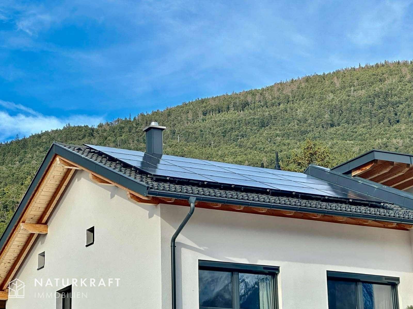 Seitenansicht des Hauses mit Solarpaneelen auf dem Dach und grüner Berglandschaft.