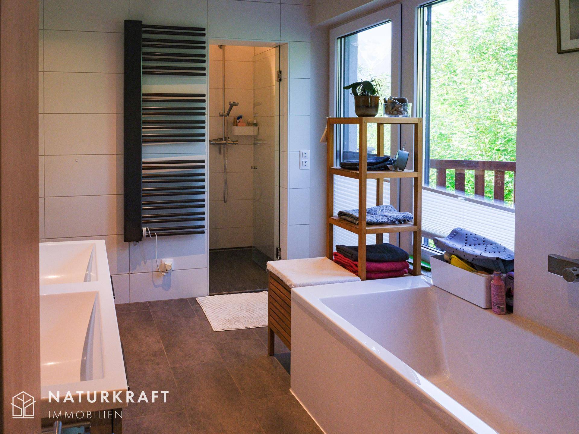 Helles Badezimmer mit Badewanne, Dusche und beheiztem Handtuchhalter, mit Zugang zum Balkon.