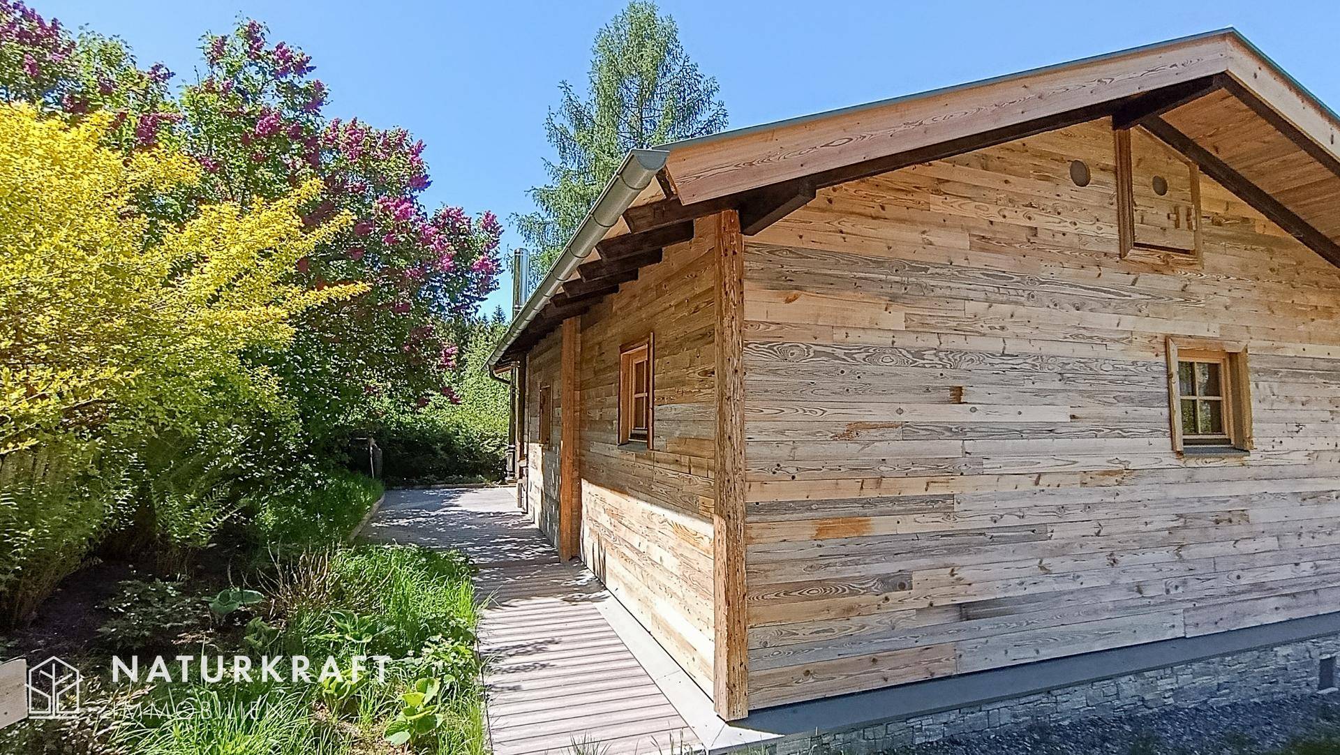 Seitenansicht des Holzchalets mit Holzfassade und einem kleinen Weg durch die Vegetation.