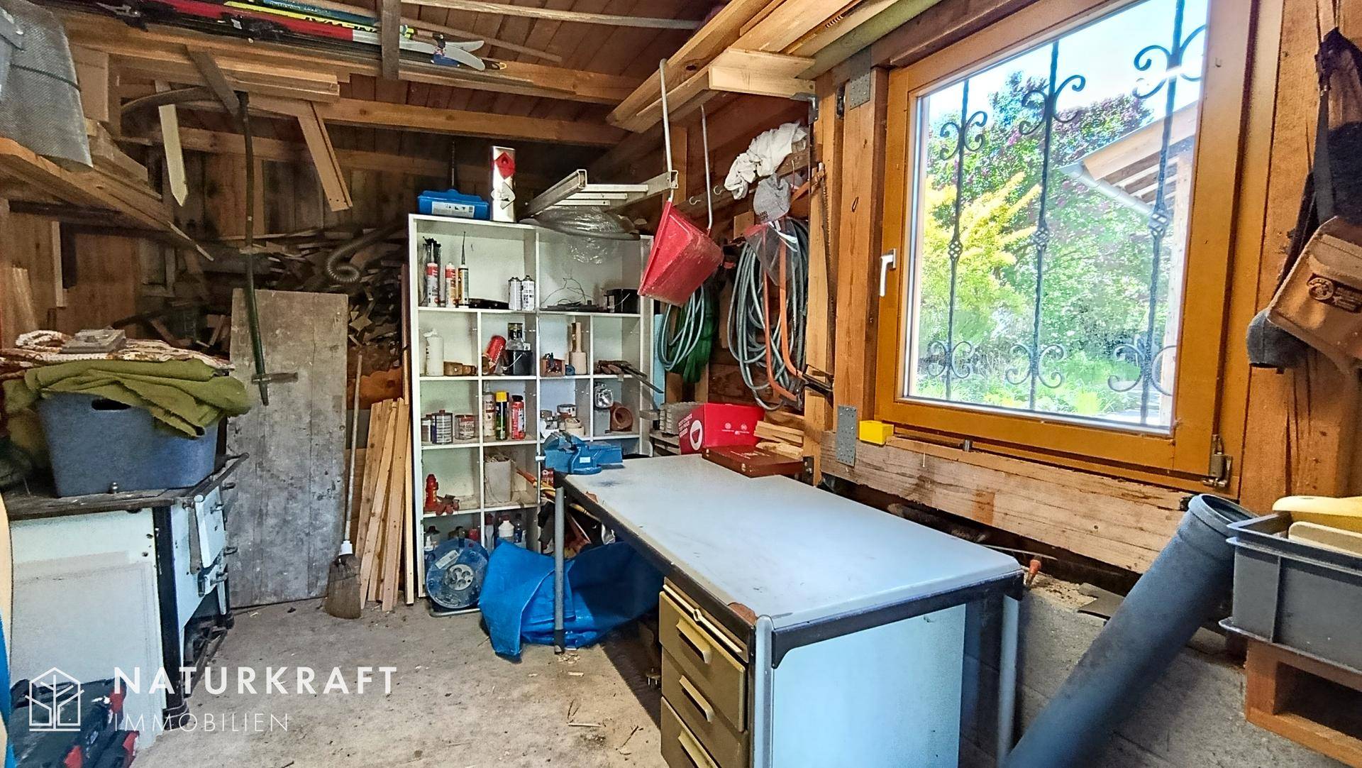 Geräumige Werkstatt oder Abstellraum mit Werkbank, Regalen und Fenster zur Natur.
