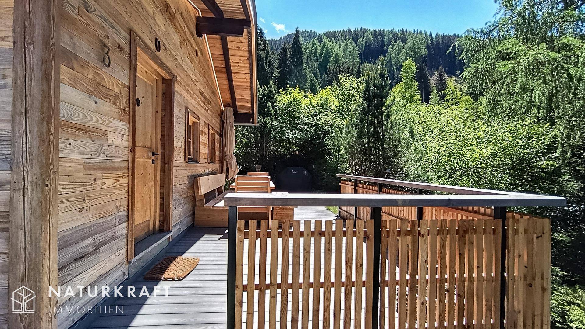 Holzterrasse mit rustikalem Geländer und weitem Blick auf die umliegende Waldlandschaft.