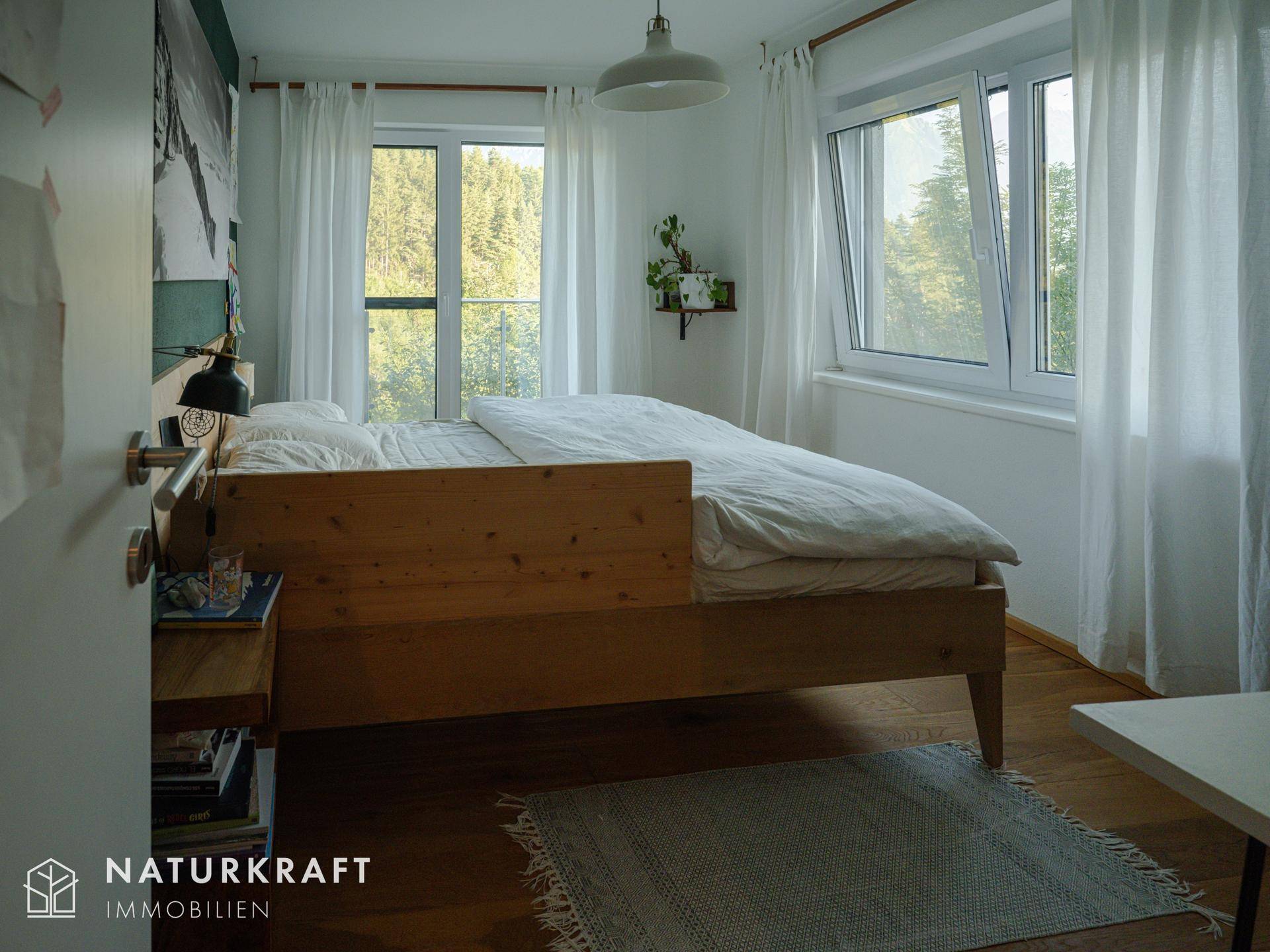 Schlafzimmer mit Holzbett, großen Fenstern und Blick ins Grüne, hell und freundlich.