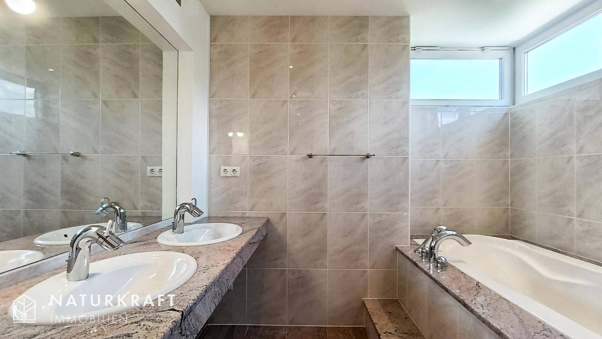 Geräumiges Badezimmer mit Doppelwaschbecken, großer Badewanne und hellen Fliesen.