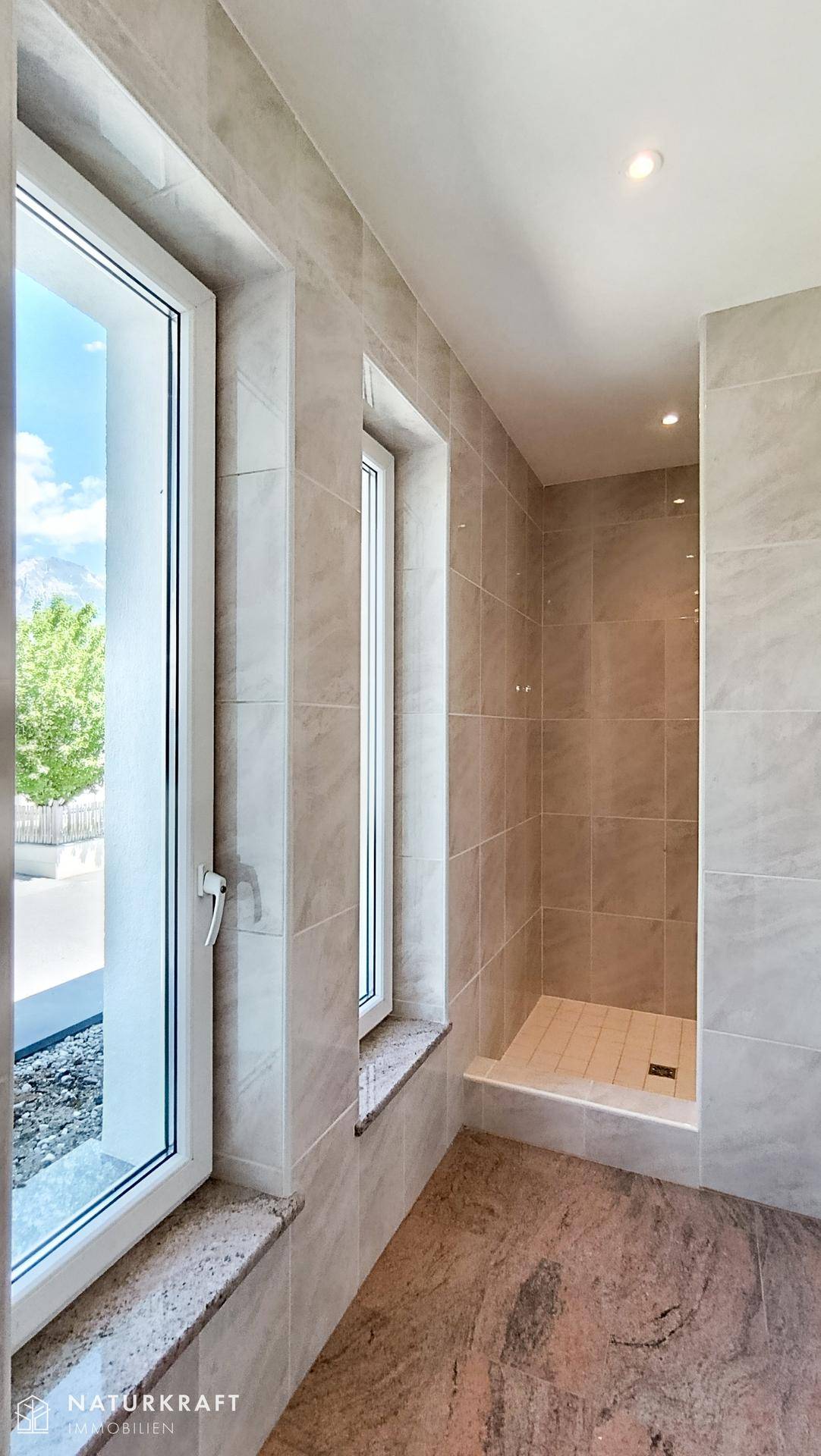 Modernes Badezimmer mit ebenerdiger Dusche, großen Fenstern und hellen Fliesen.