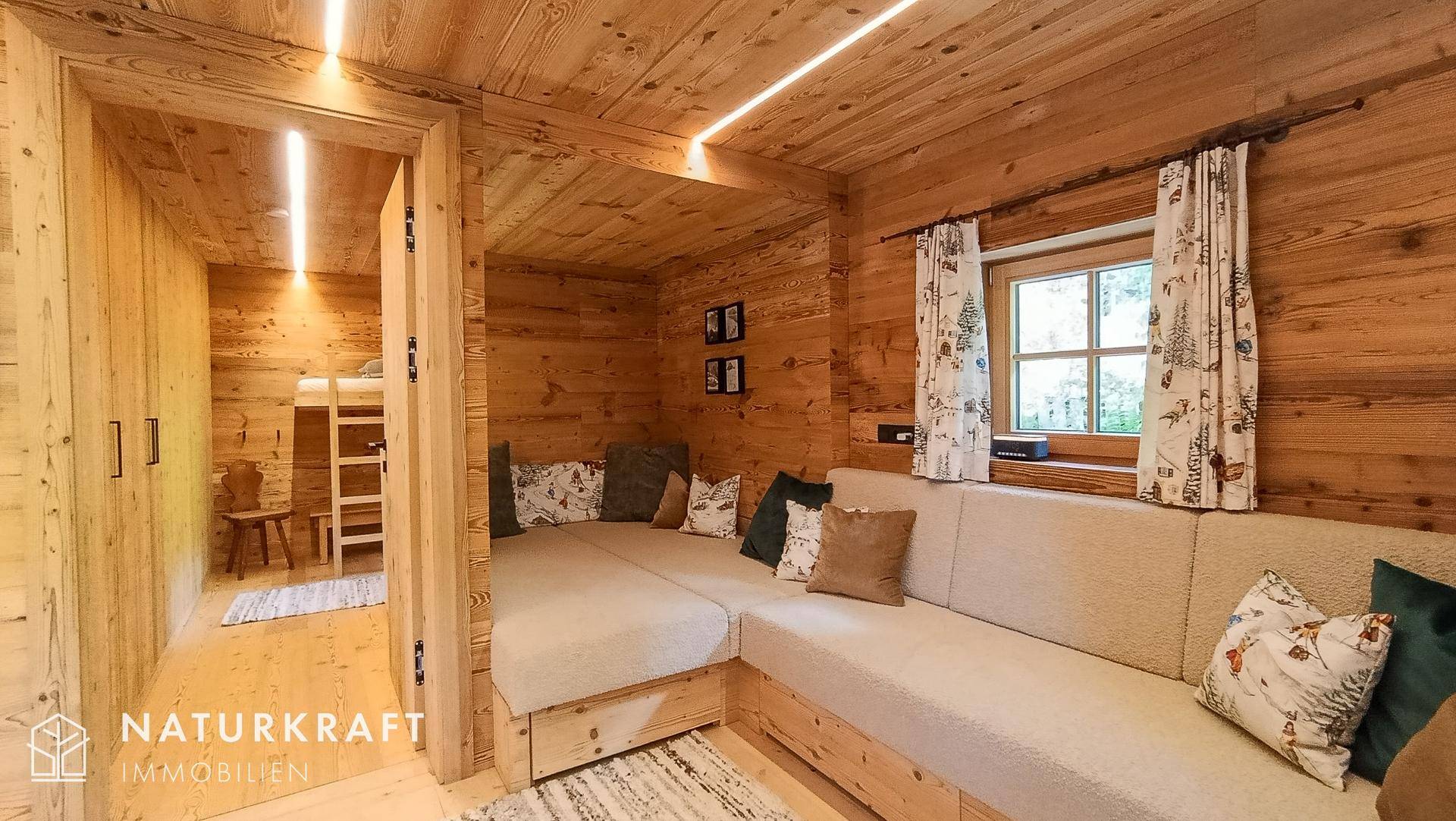 Wohnbereich mit bequemer Sitzecke, Holzwänden und Zugang zu einem weiteren Zimmer.