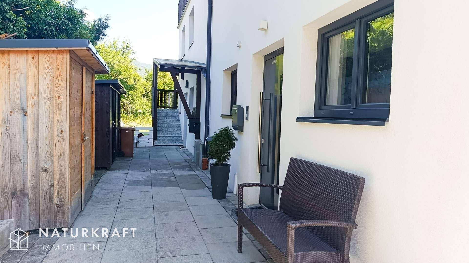 Seitlicher Zugang zum Haus mit gepflastertem Weg, Sitzbank und Holzschuppen.