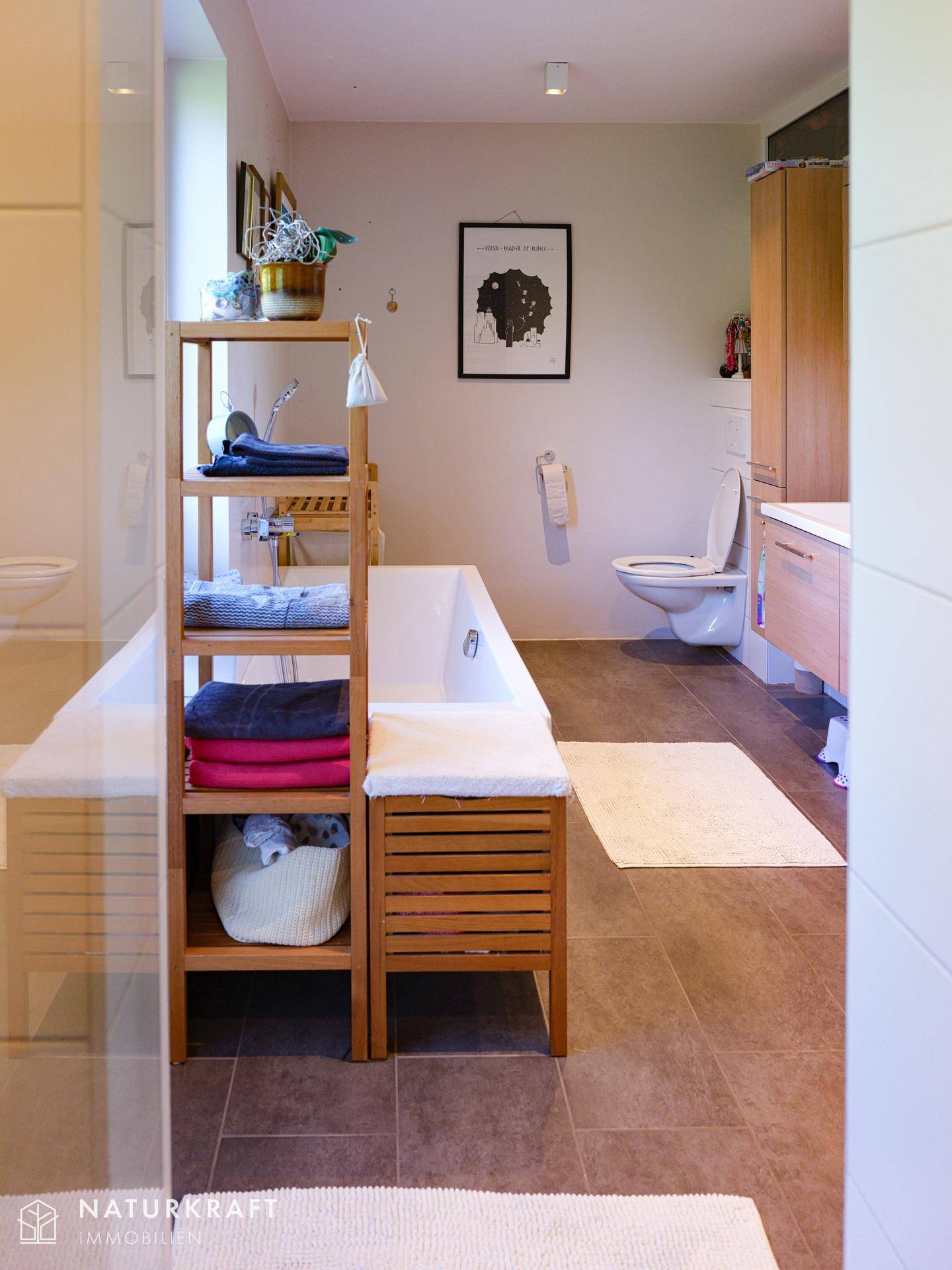 Modernes Badezimmer mit Badewanne, wandhängendem WC und Holzregal für Handtücher.