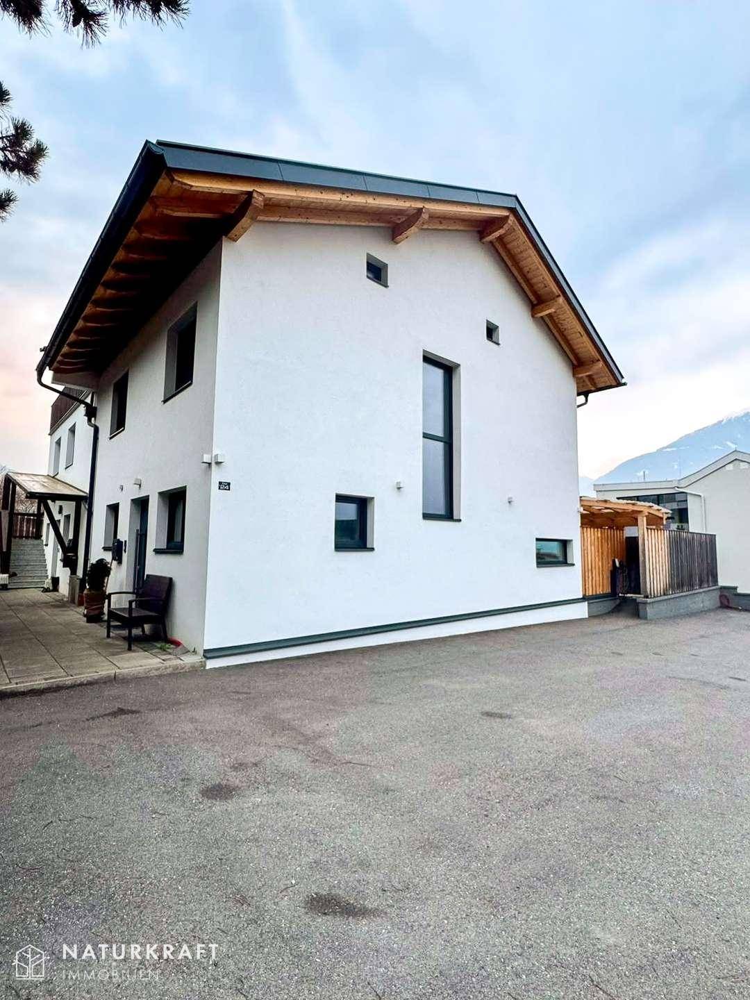 Moderne Architektur des Hauses mit weißer Fassade und Holzdachüberstand unter bewölktem Himmel.