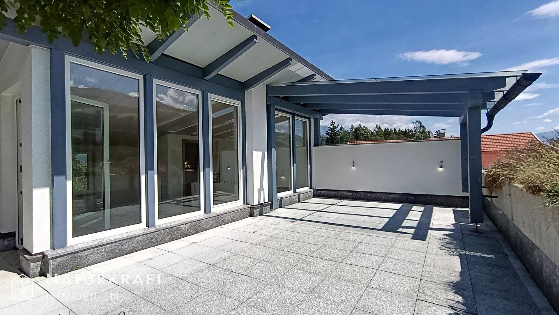 Geräumige Terrasse mit Überdachung, Fliesenboden und großen Glasfronten zum Innenbereich.