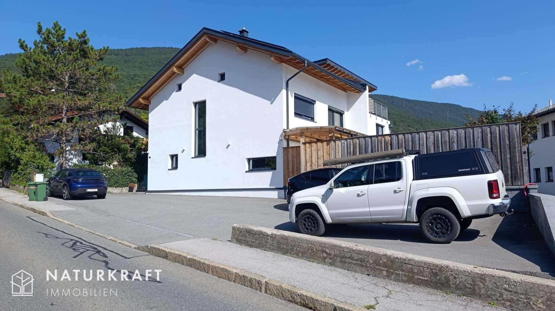 Modernes Wohnhaus mit weißer Fassade, Holzelementen und großem Außenbereich an einem sonnigen Tag.