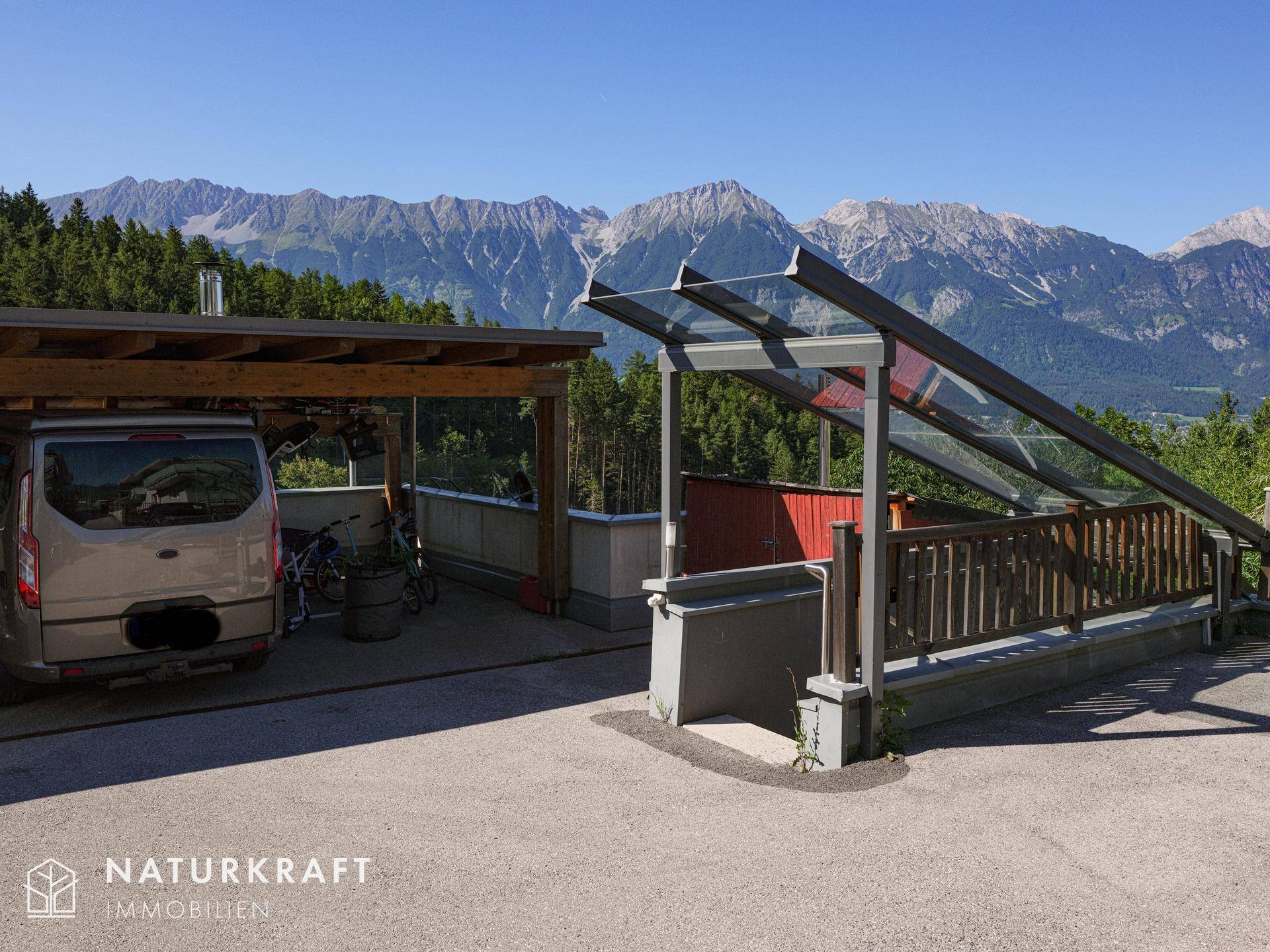Außenbereich mit Carport und überdachtem Zugang, umgeben von Bergen und Wald.