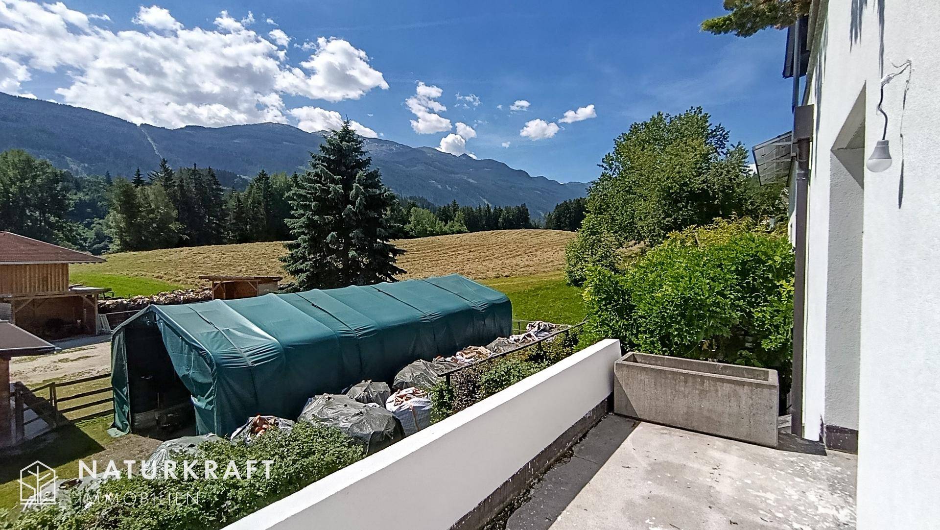 Ländliche Umgebung mit Blick auf Berge, Felder und einen Gartenbereich mit Gewächshaus.