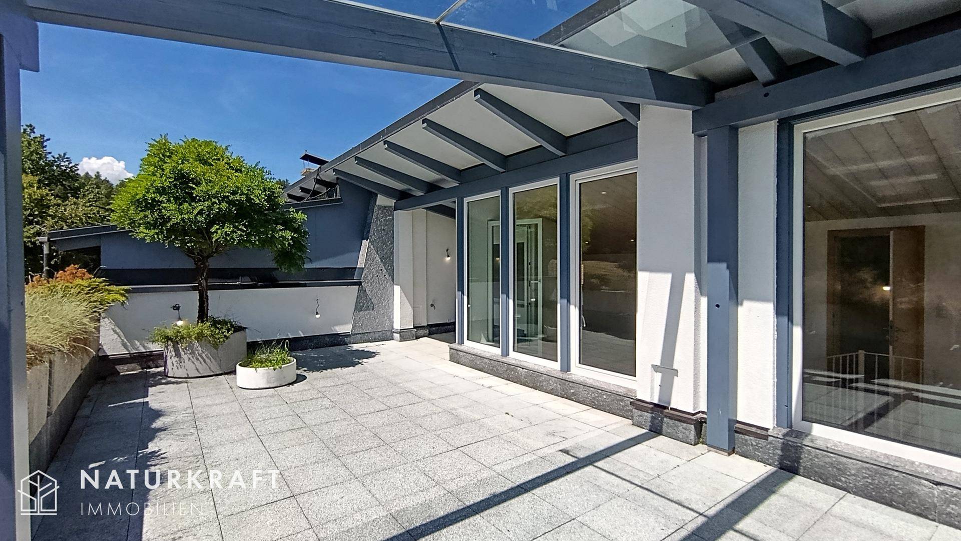 Sonnige Dachterrasse mit Fliesenboden, moderner Überdachung und Zugang zu den Innenräumen.