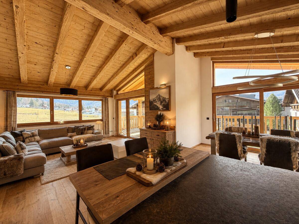Heller Wohn- und Essbereich im alpinen Stil mit Holzbalken, bequemen Sofas und weitem Blick in die Natur.